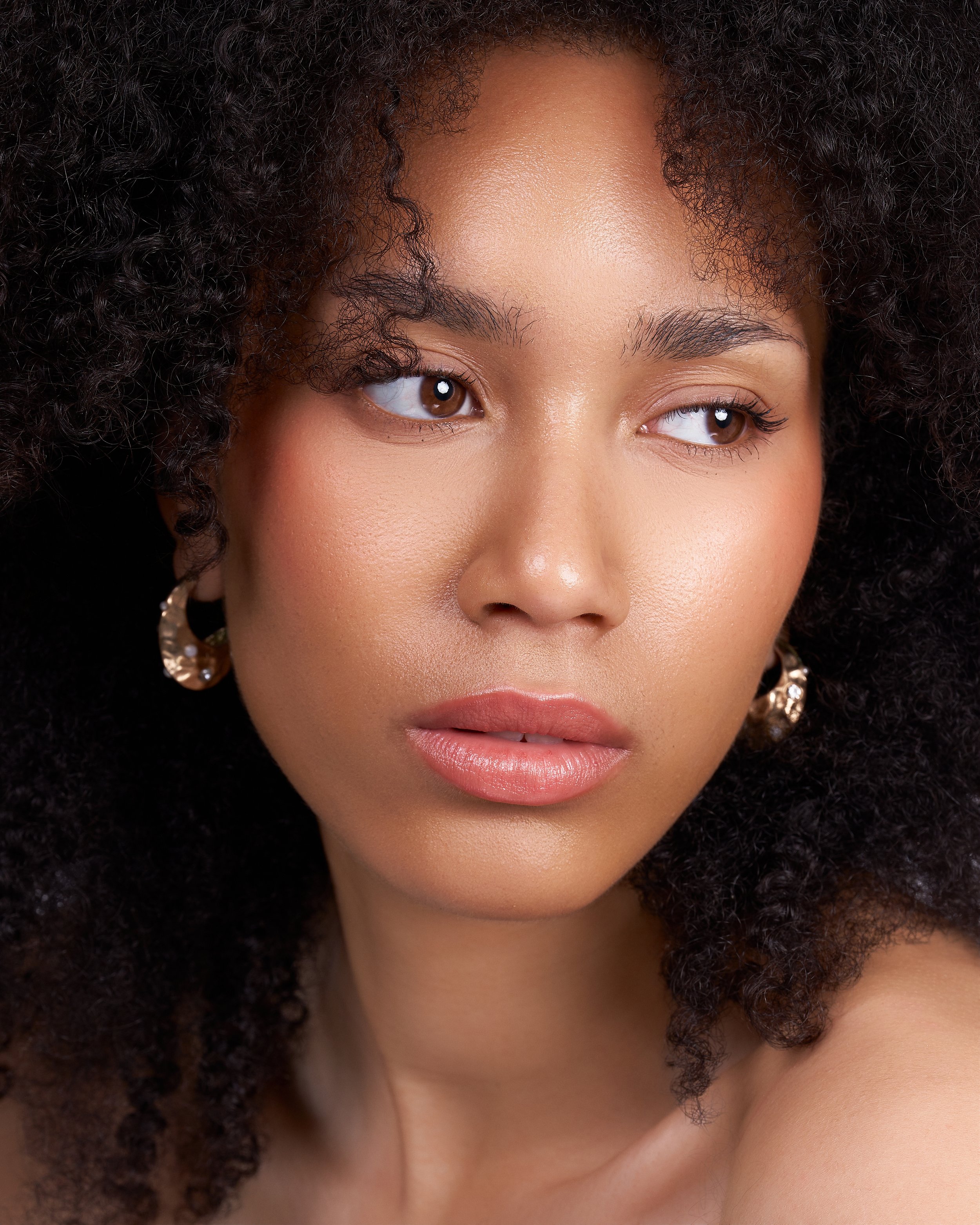 Close-up of a woman's face with natural curly hair, brown eyes, and light makeup.