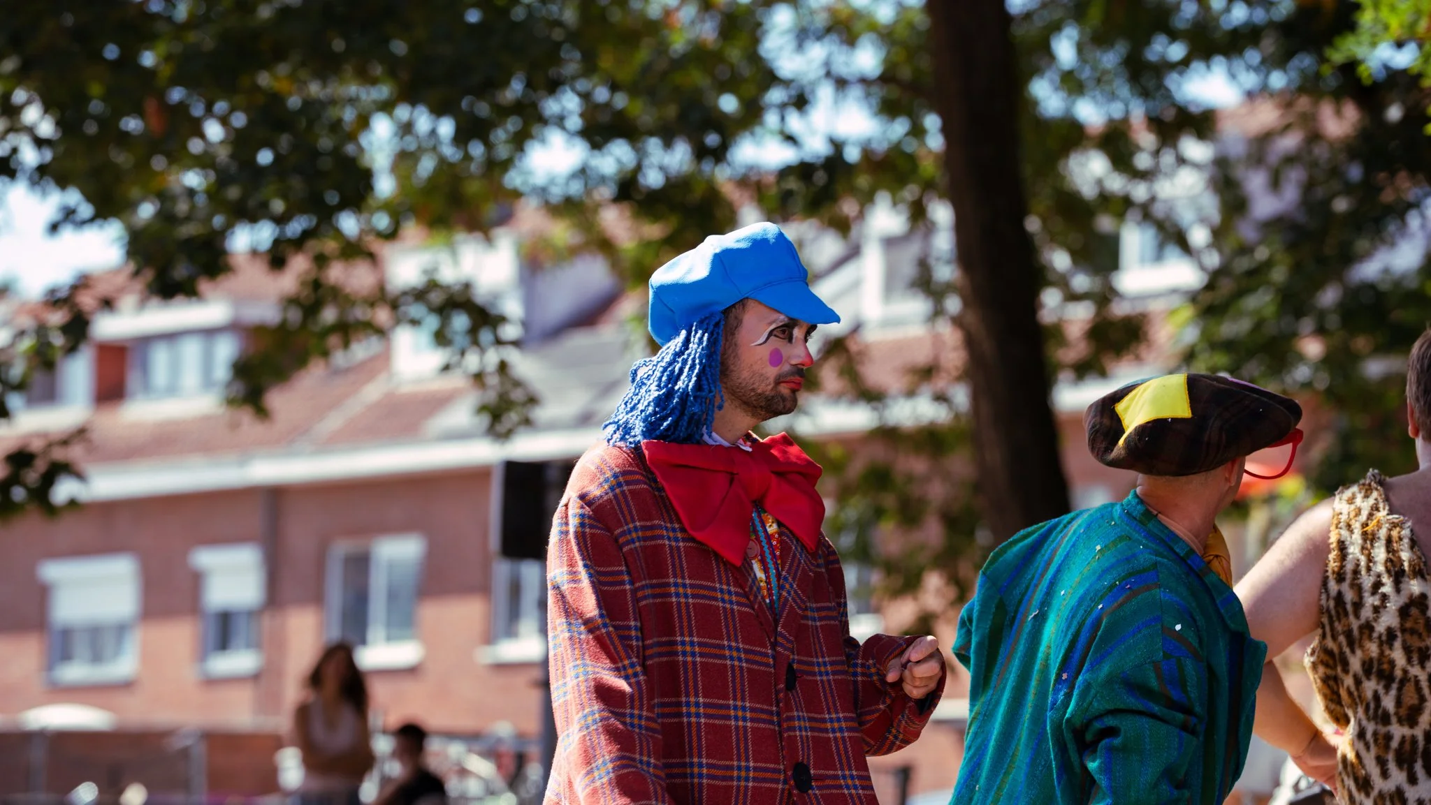 People dressed as clowns outdoors in a park during daytime, with trees and buildings in the background.
