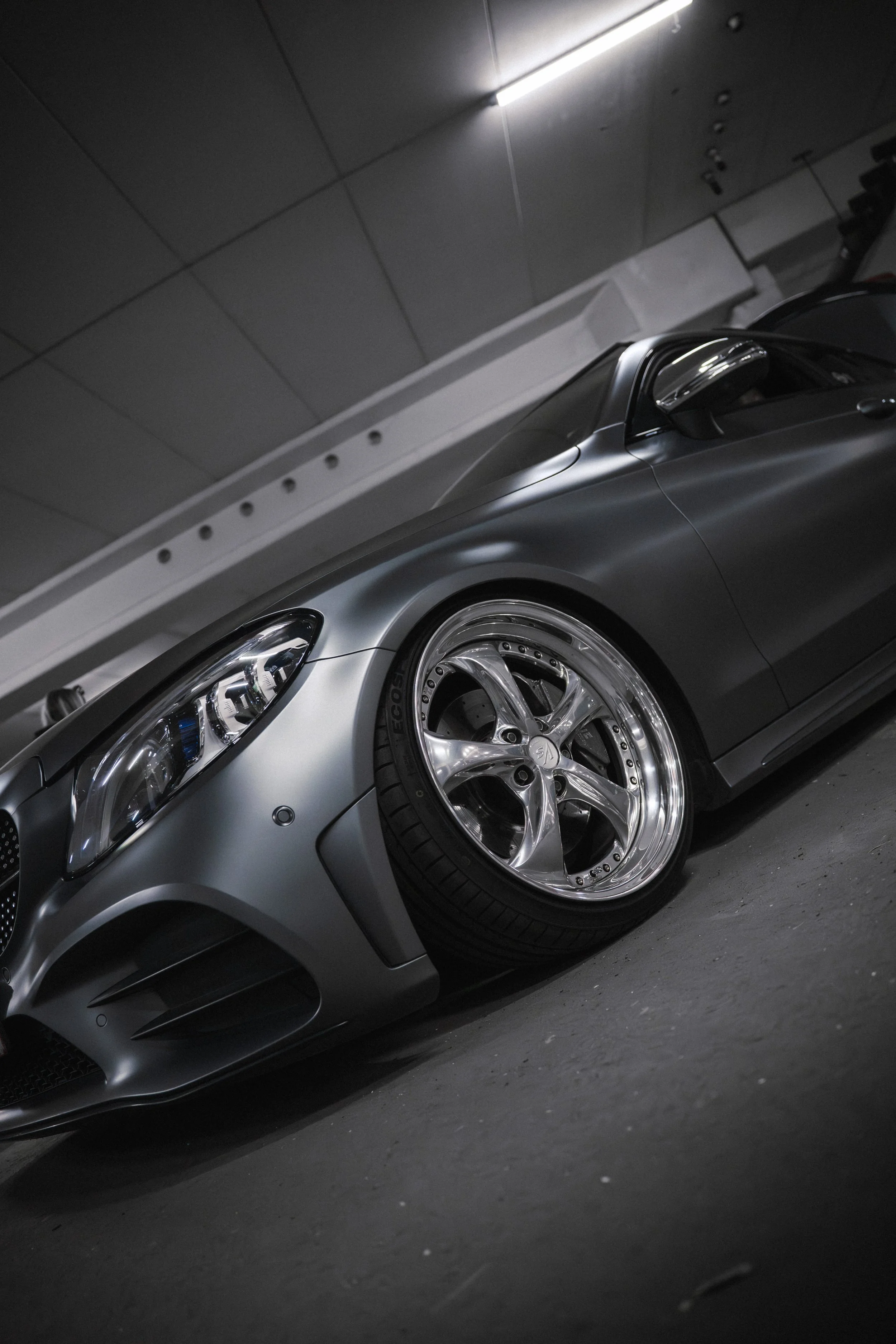 A silver sports car with custom wheels is parked in an underground parking garage.