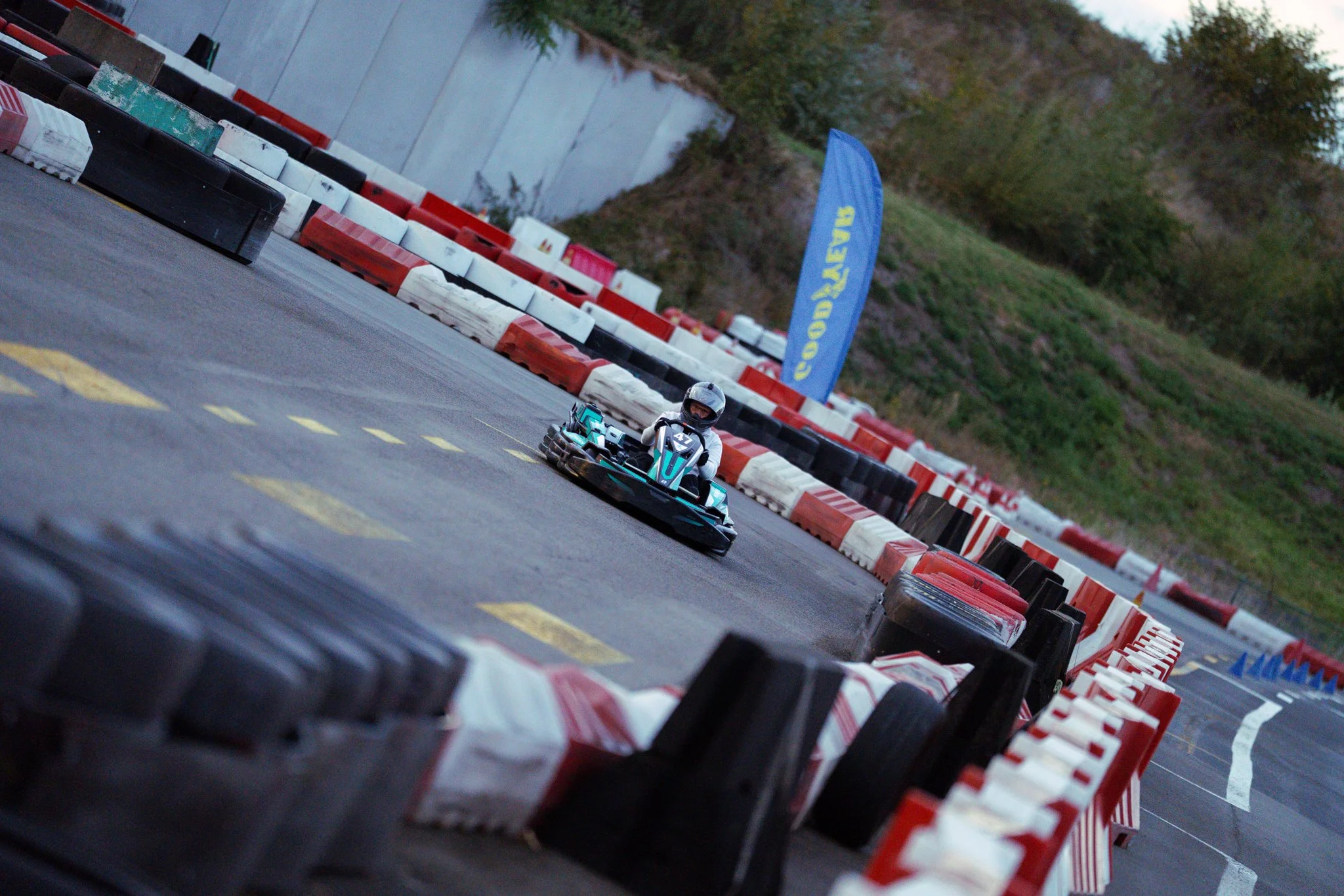 A person racing a go-kart on an outdoor track lined with red, white, and black barriers.