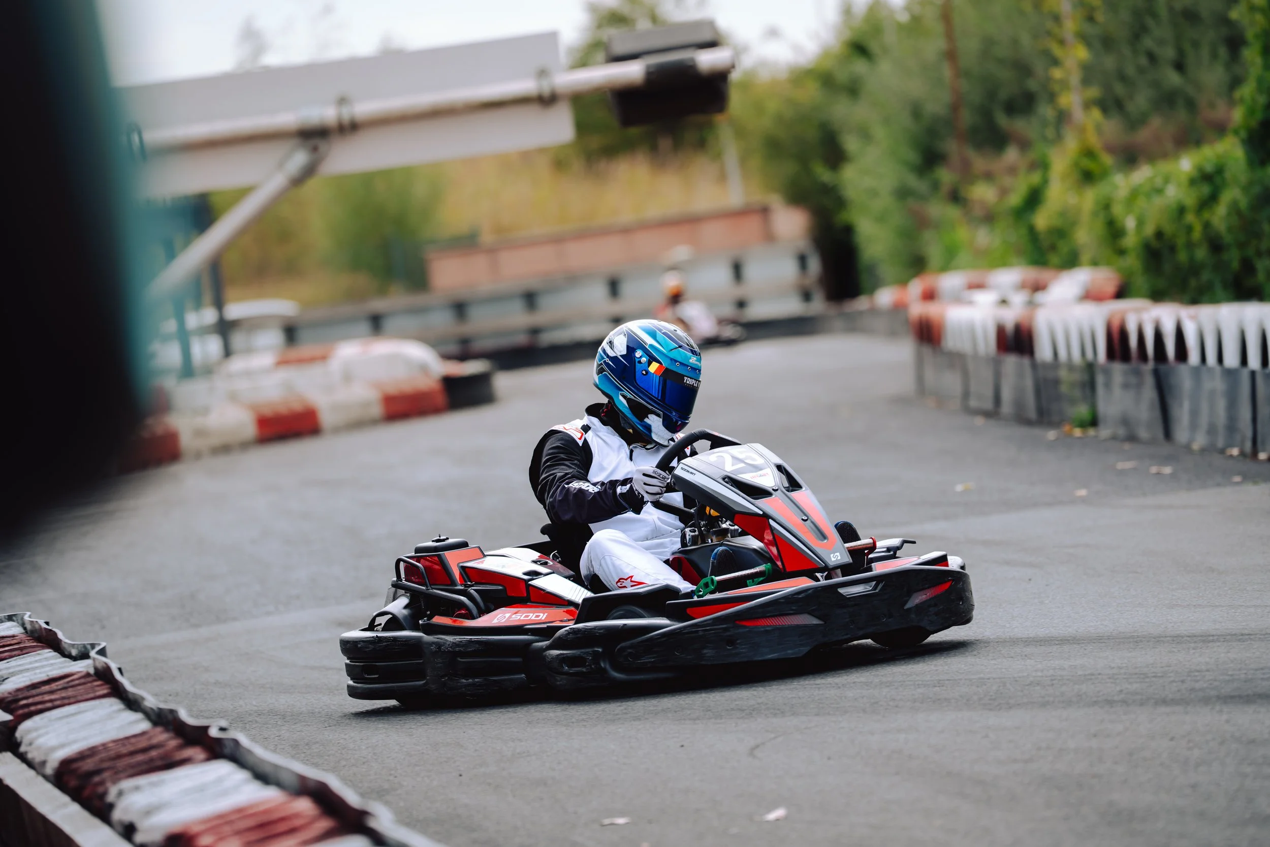 A person riding a red and black go-kart on a race track, wearing a blue helmet and black and white racing suit.