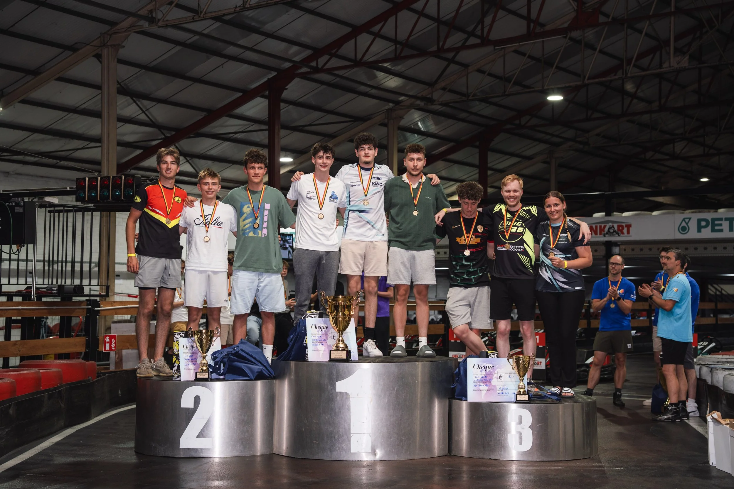Group of young athletes standing on a winners' podium holding medals and trophies after a race at an indoor sports arena.