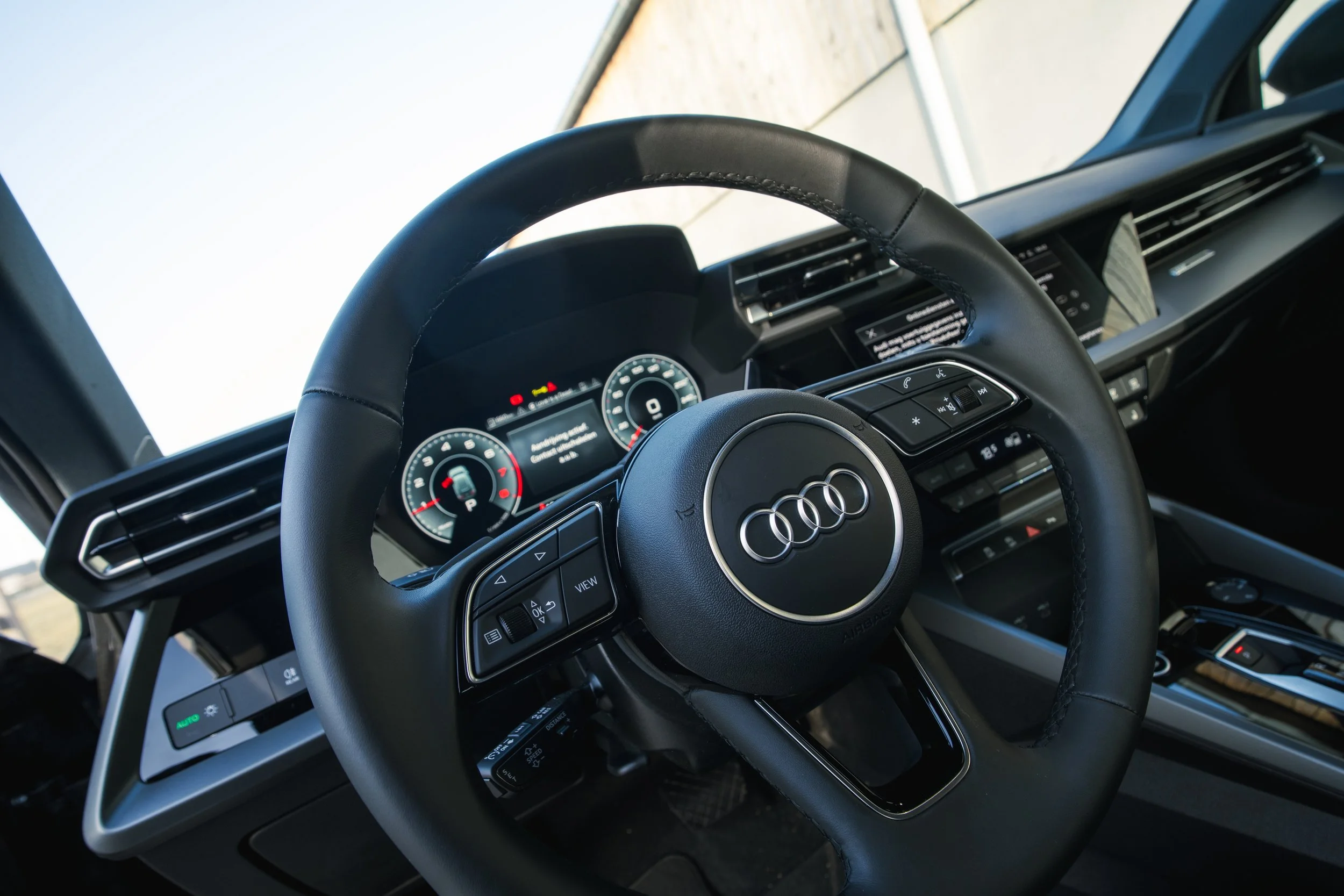 Interior of an Audi vehicle, showing the steering wheel with the Audi logo, digital dashboard display, and central console with controls.