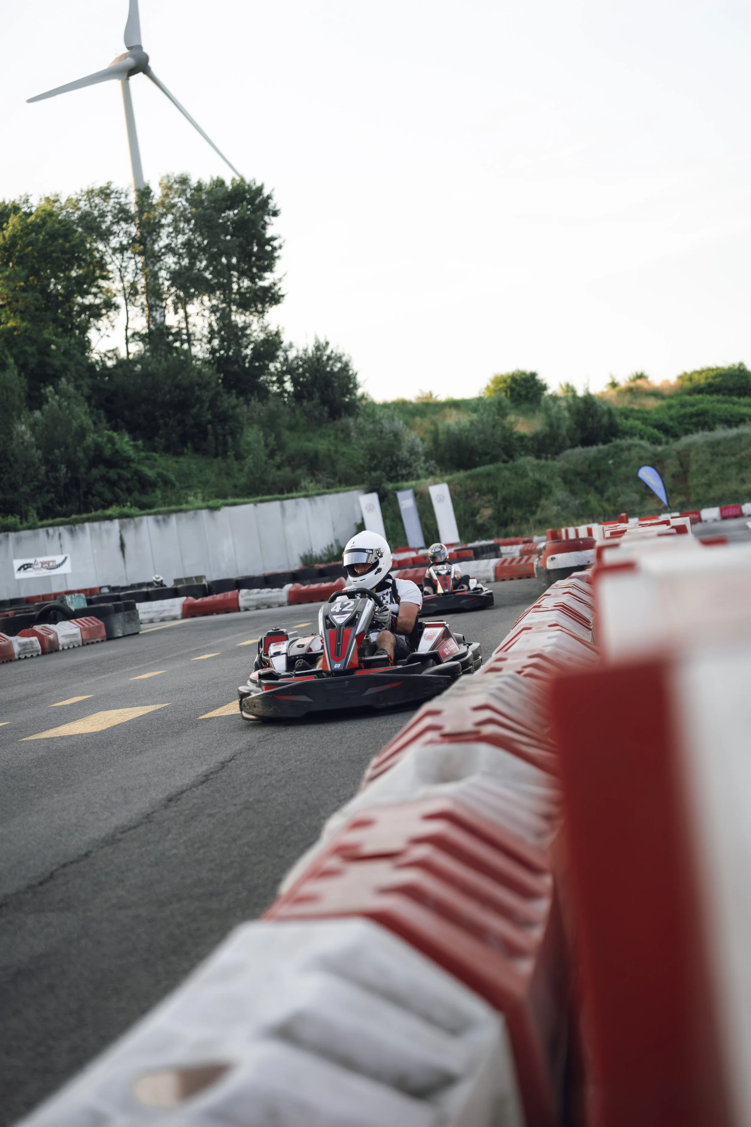 People racing go-karts on an outdoor track with safety barriers and trees in the background.