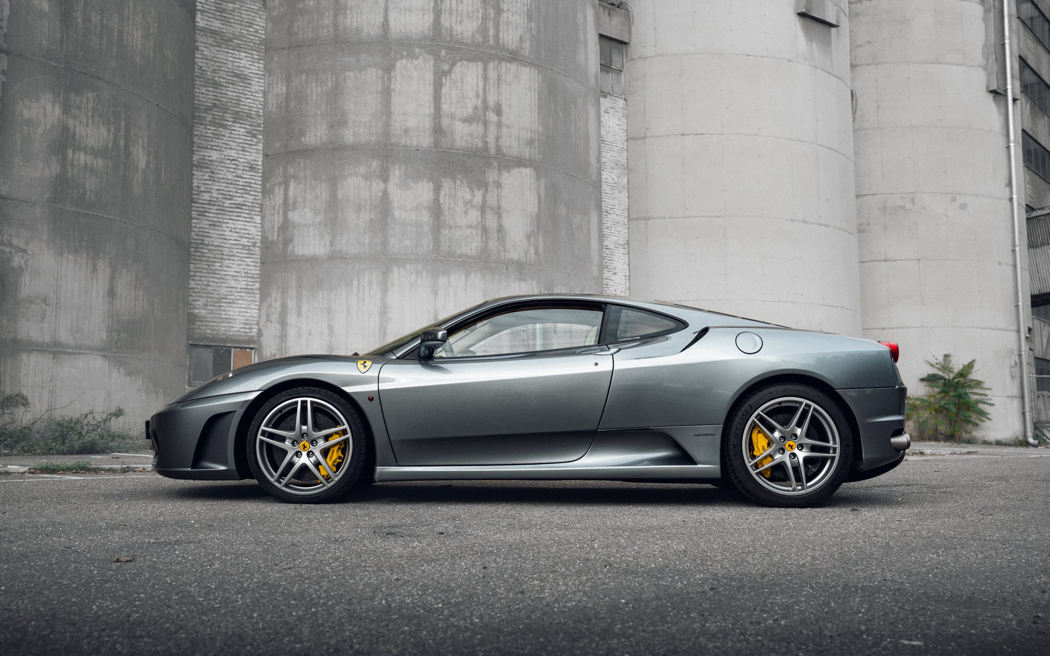 Silver Ferrari sports car parked on urban street with concrete buildings in the background.