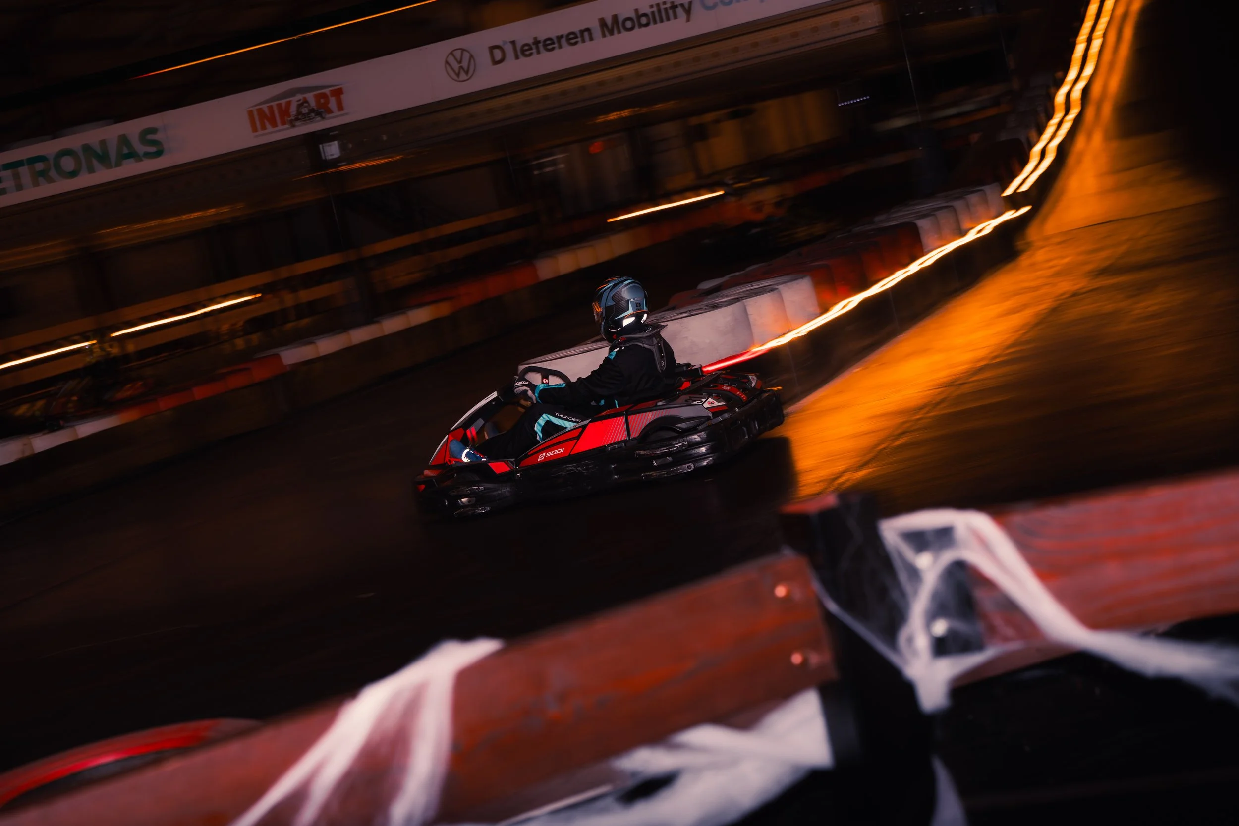 A person riding a jet ski on the water at night, with orange trails of light behind them, blurred motion, and a bridge with signage in the background.