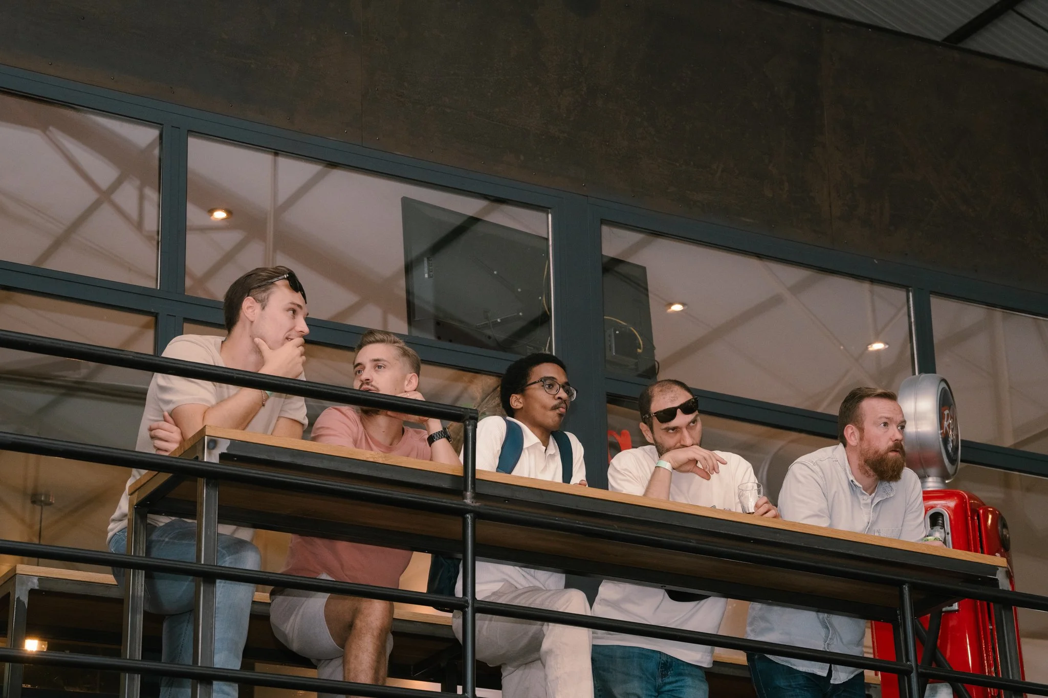 Five men sitting at a table in a modern indoor space, engaged in conversation and listening attentively.