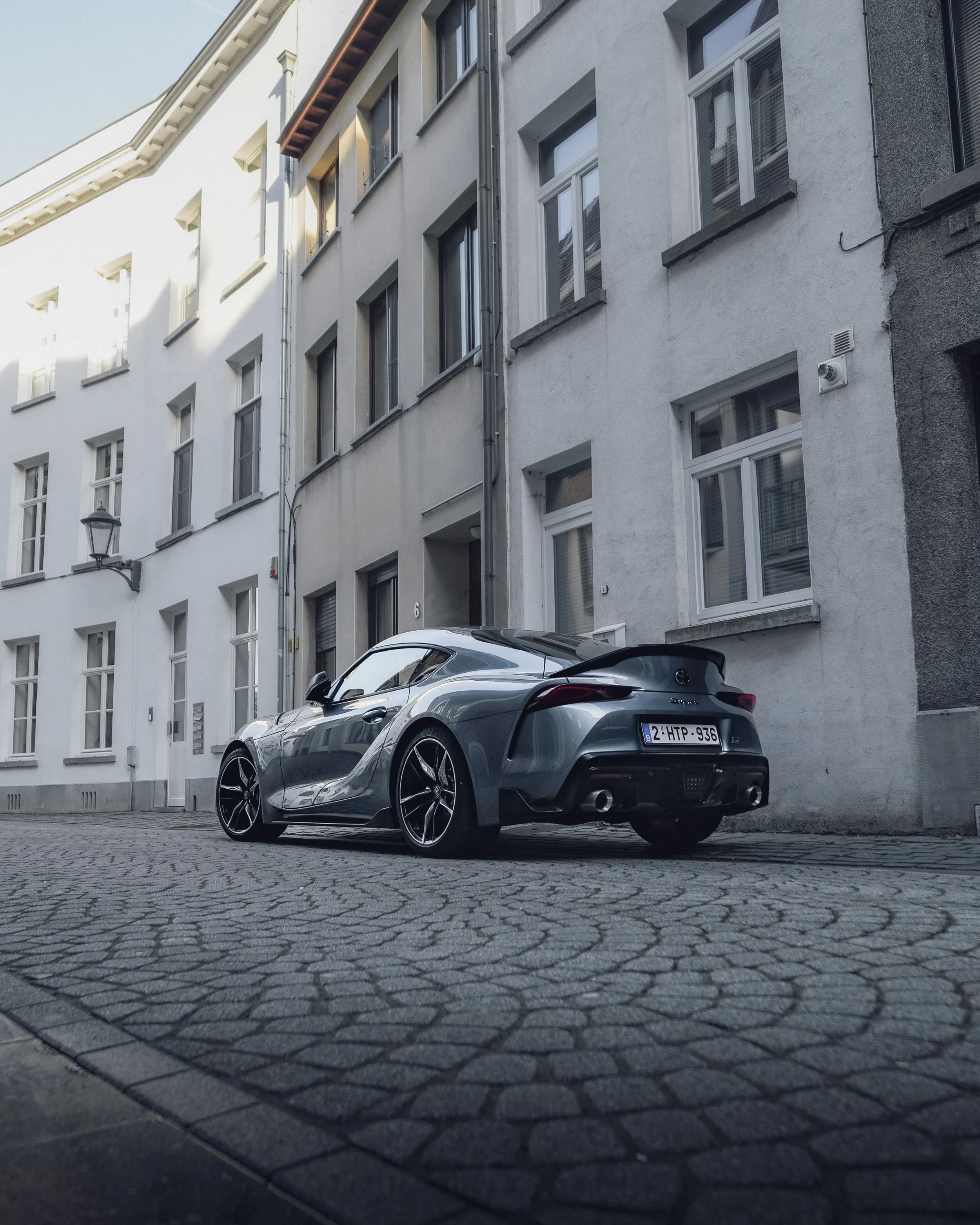 A sleek, gray sports car parked on a cobblestone street in front of residential buildings.
