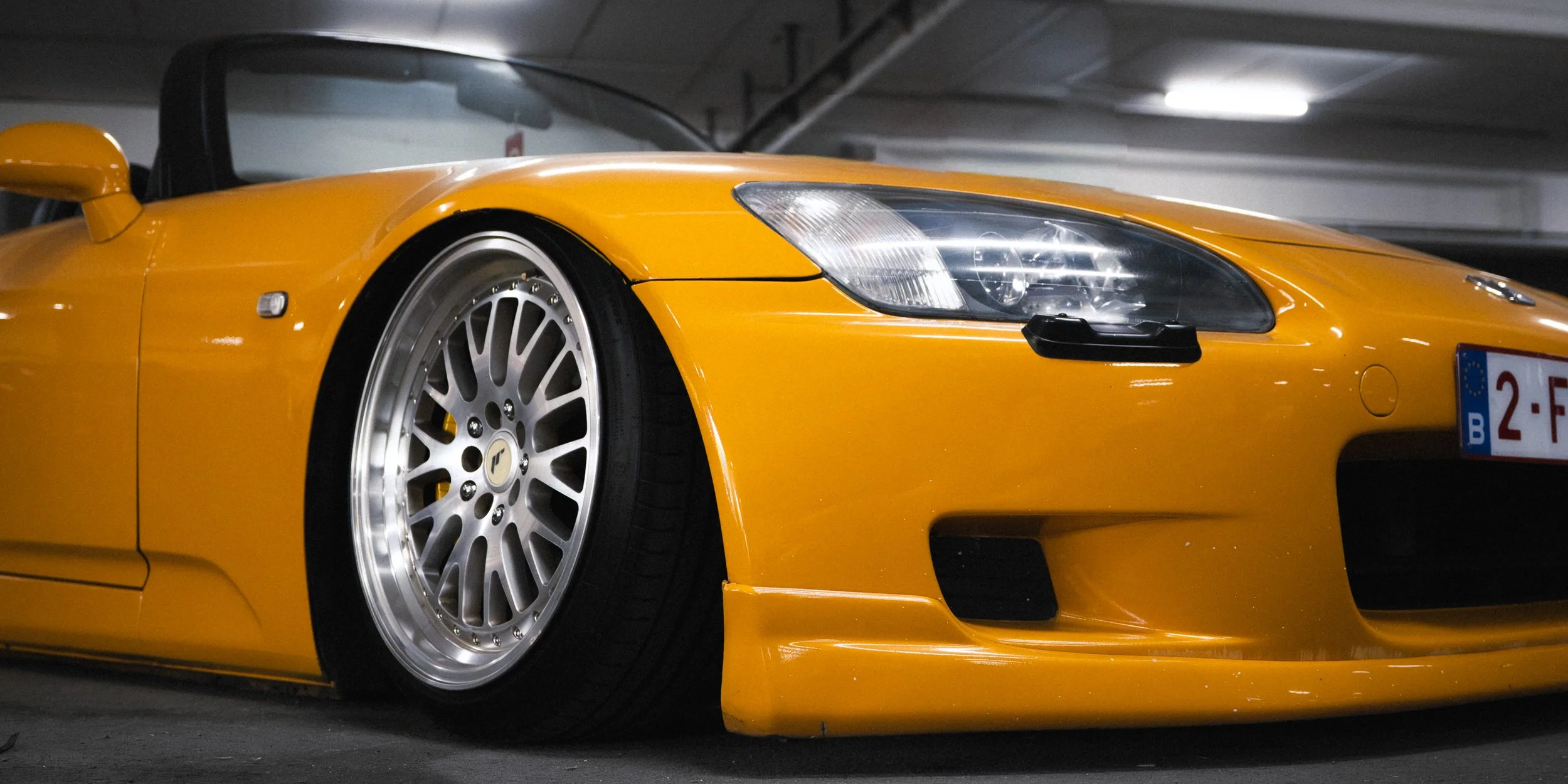 A yellow sports car with large silver wheels parked in an indoor parking garage.