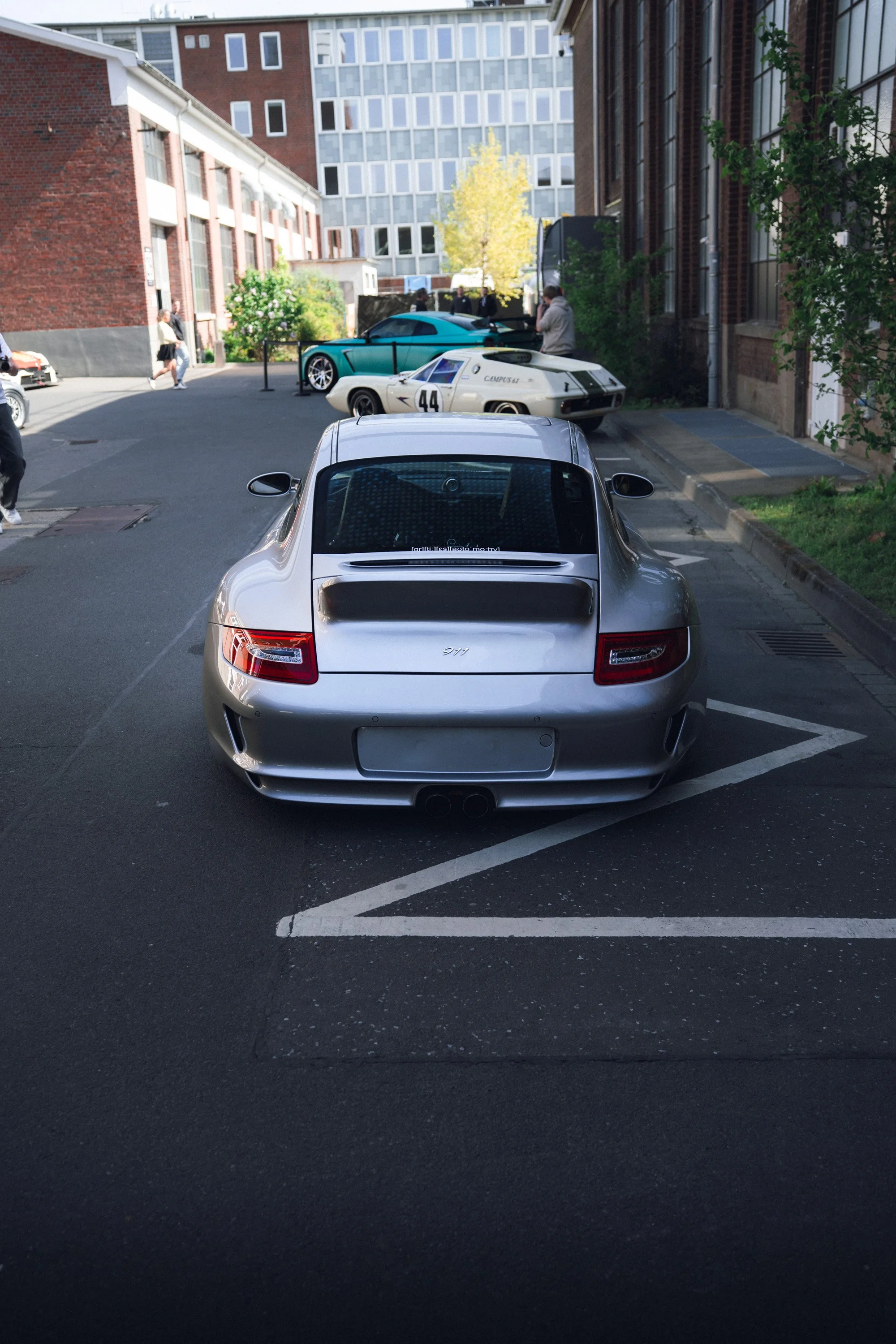 Back view of a silver Porsche 911 parked in a parking lot.