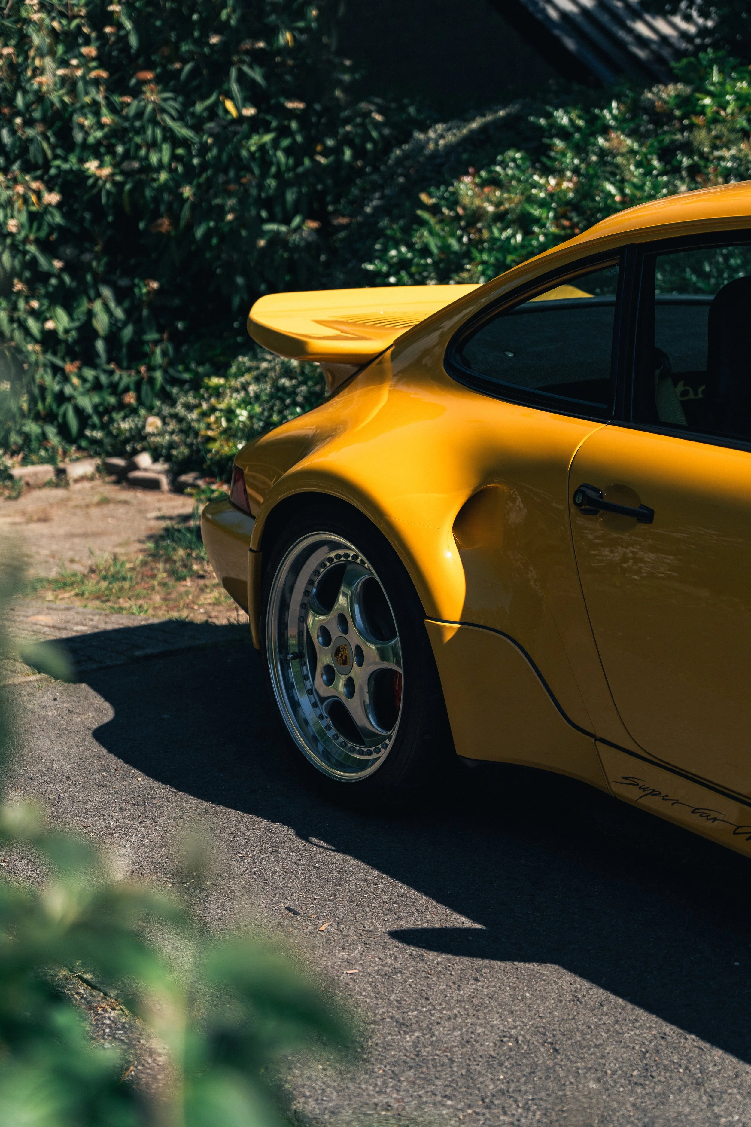 Yellow sports car with a rear spoiler, parked on the street next to greenery.