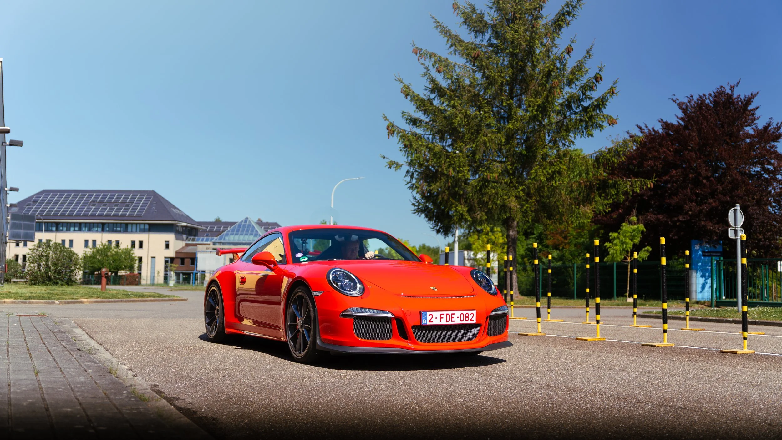 Red Porsche sports car parked on a street with trees and modern buildings in the background.