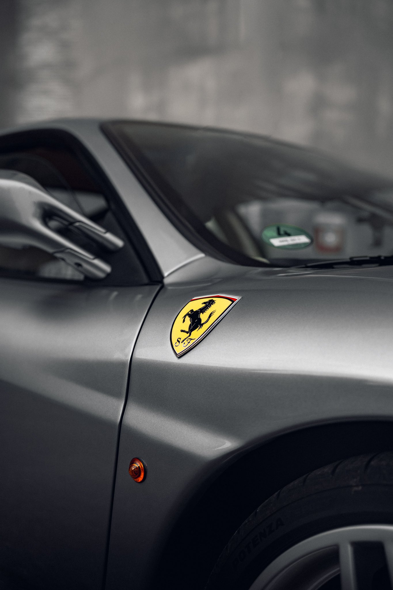 Close-up of a silver Ferrari car showing the iconic Ferrari logo on the front fender and part of the wheel.