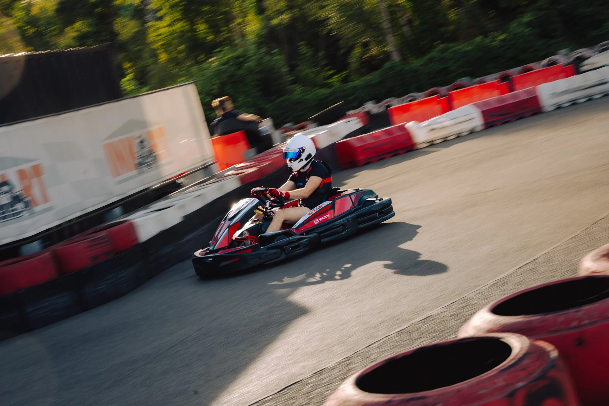 Person riding a go-kart on an outdoor track with safety barriers and trees in the background.