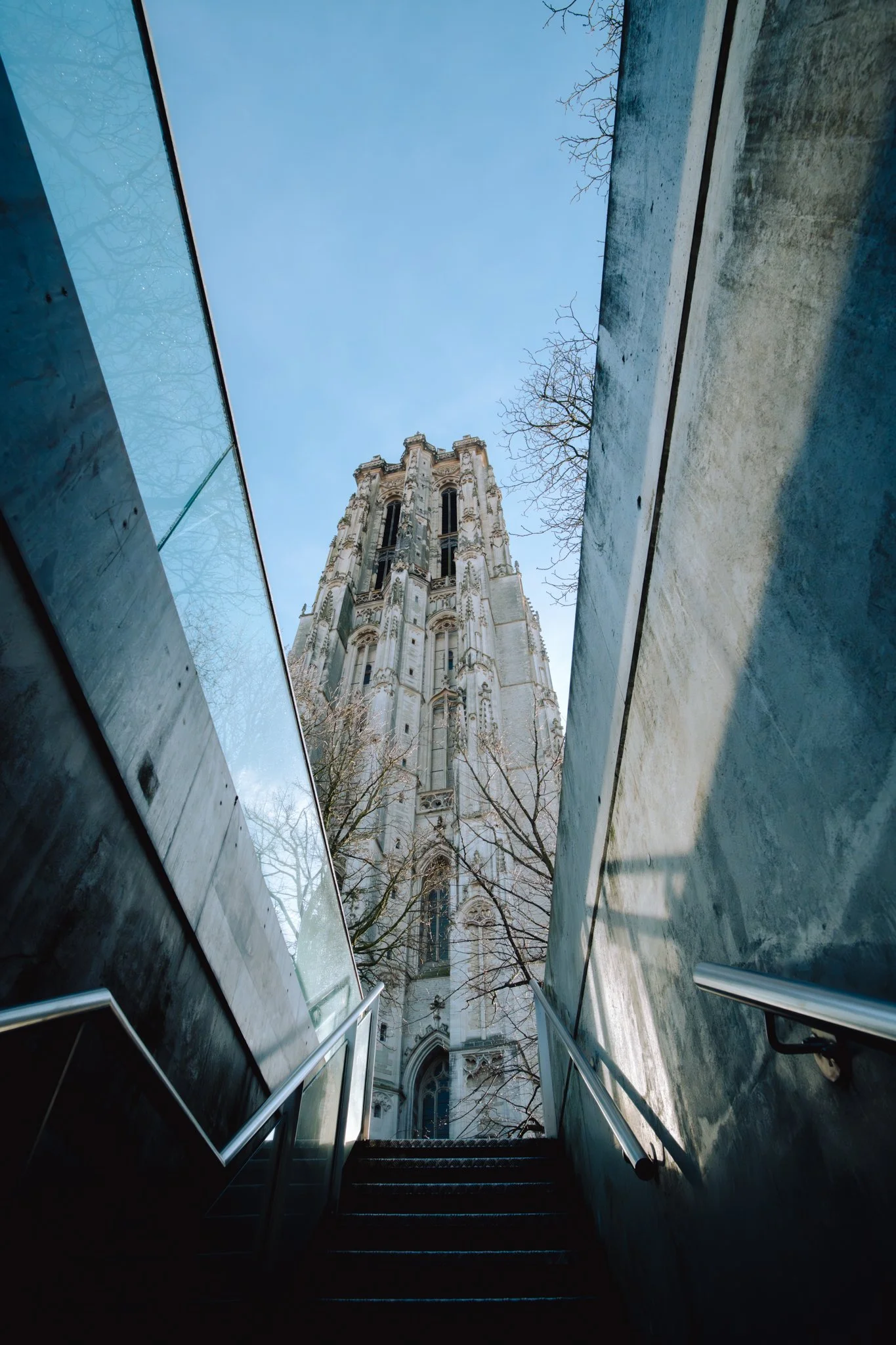View of a tall, historic cathedral viewed from a staircase with modern glass and metal walls on either side.