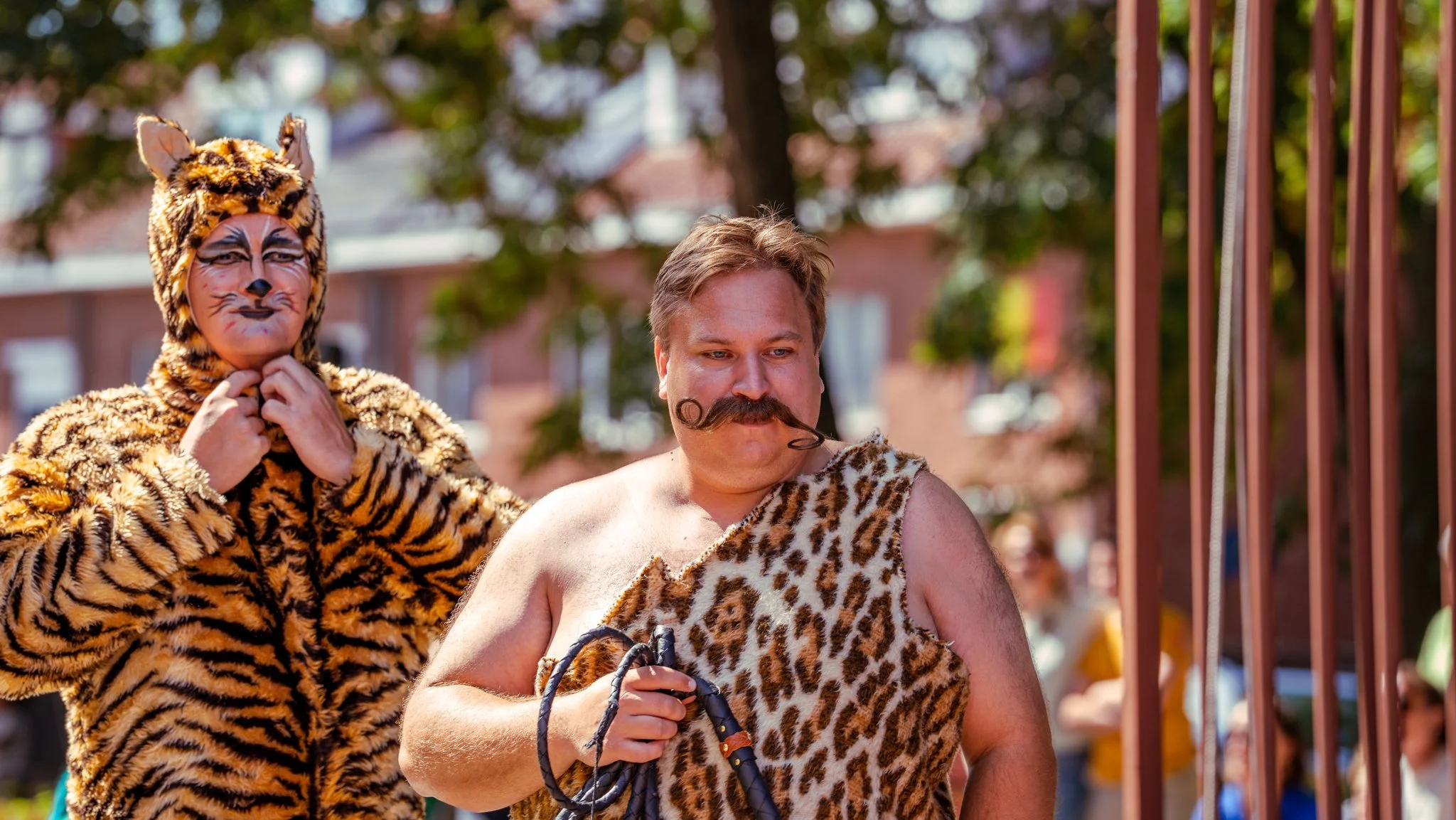 People dressed in animal costume and caveman attire during a festival or parade, with trees and buildings in the background.