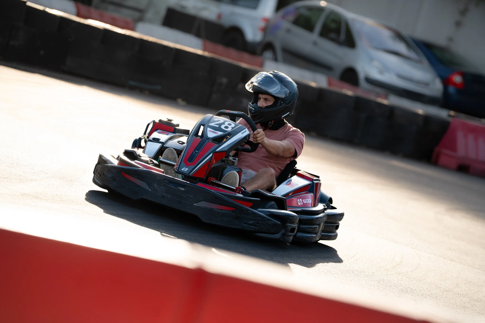 A person riding a go-kart on a track, wearing a helmet and a pink t-shirt.