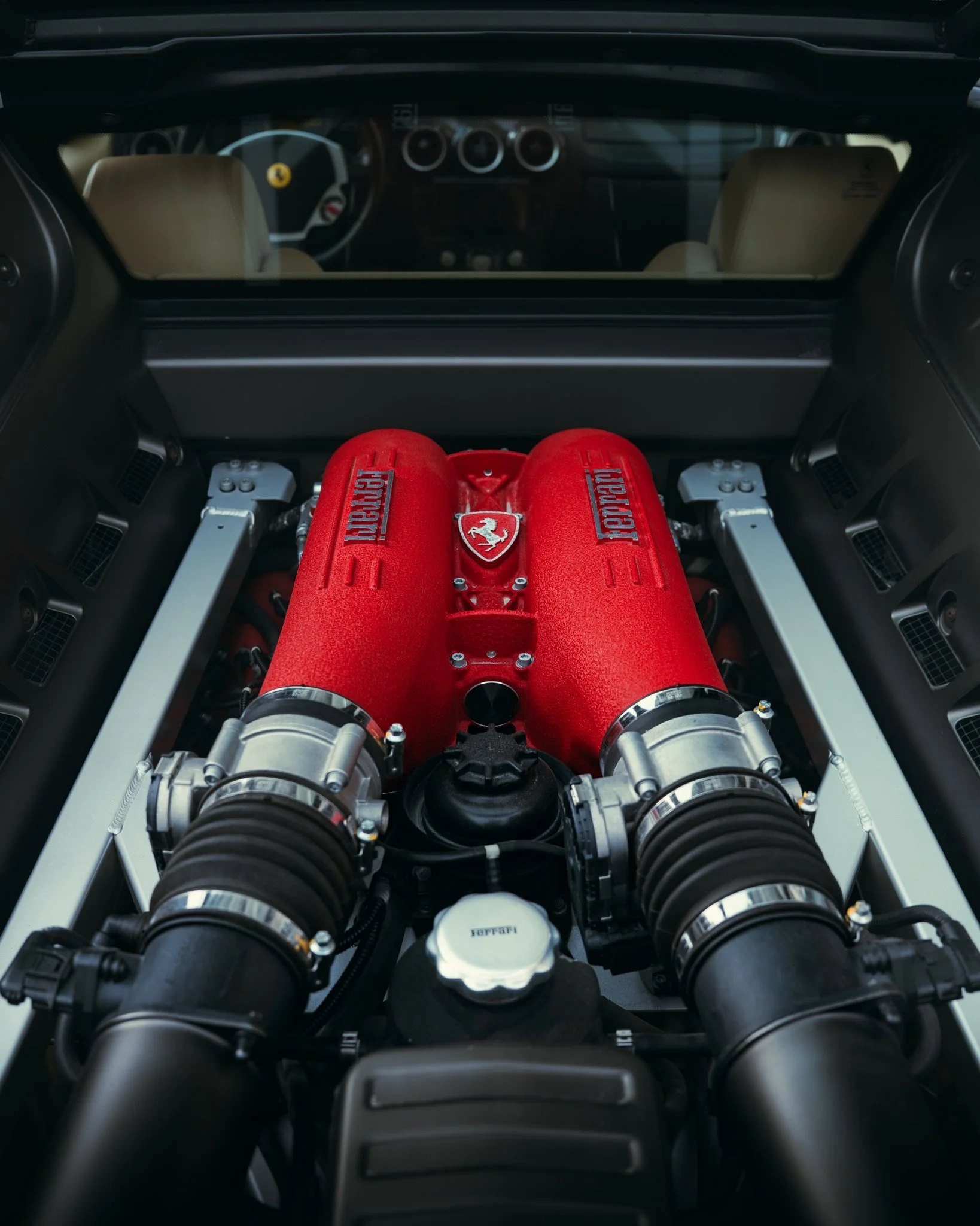 View inside a Ferrari with a red engine cover, visible Ferrari logo, and racing seats in the background.