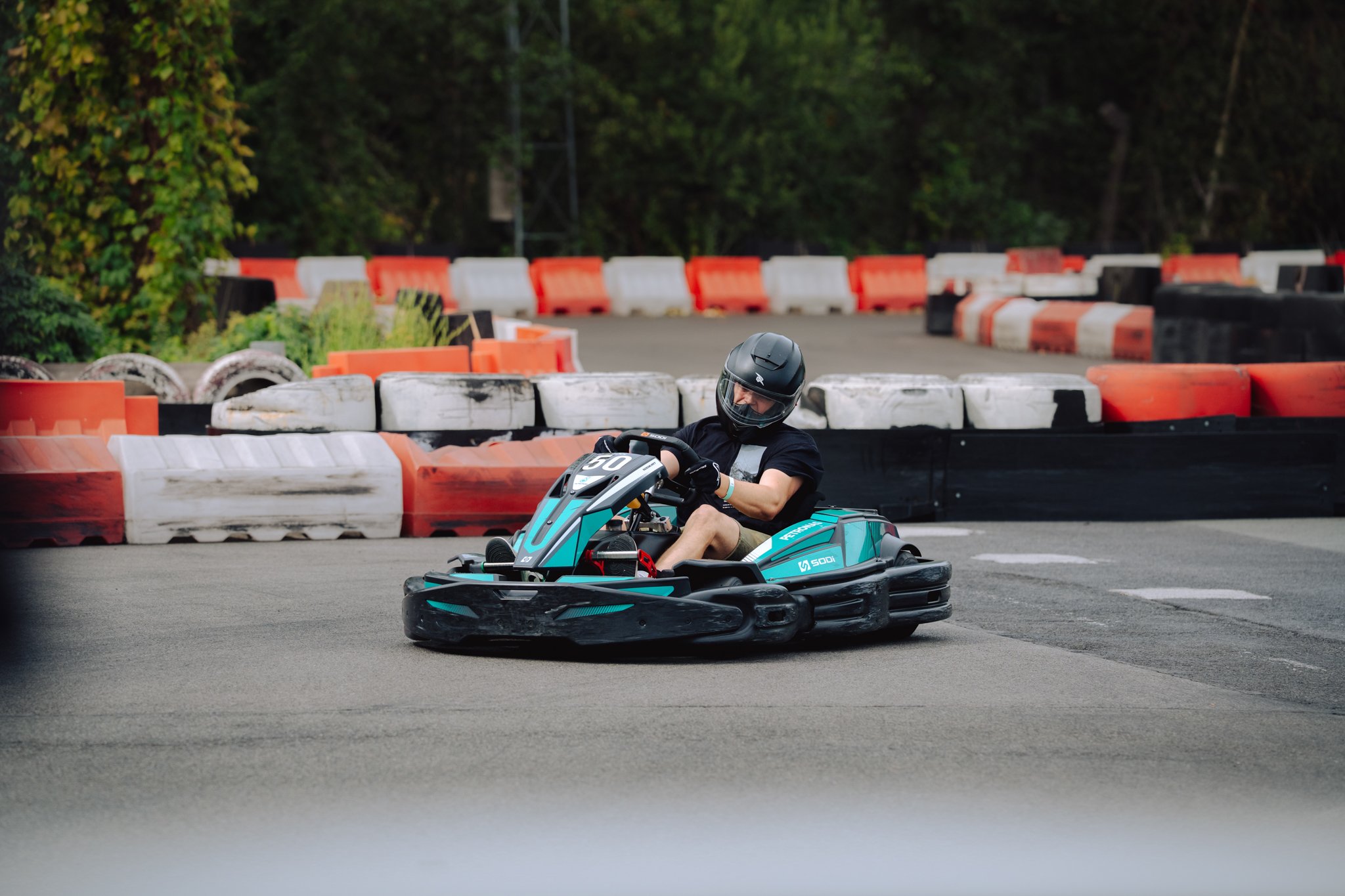 Person riding a go-kart on an outdoor race track, wearing a black helmet and black t-shirt.