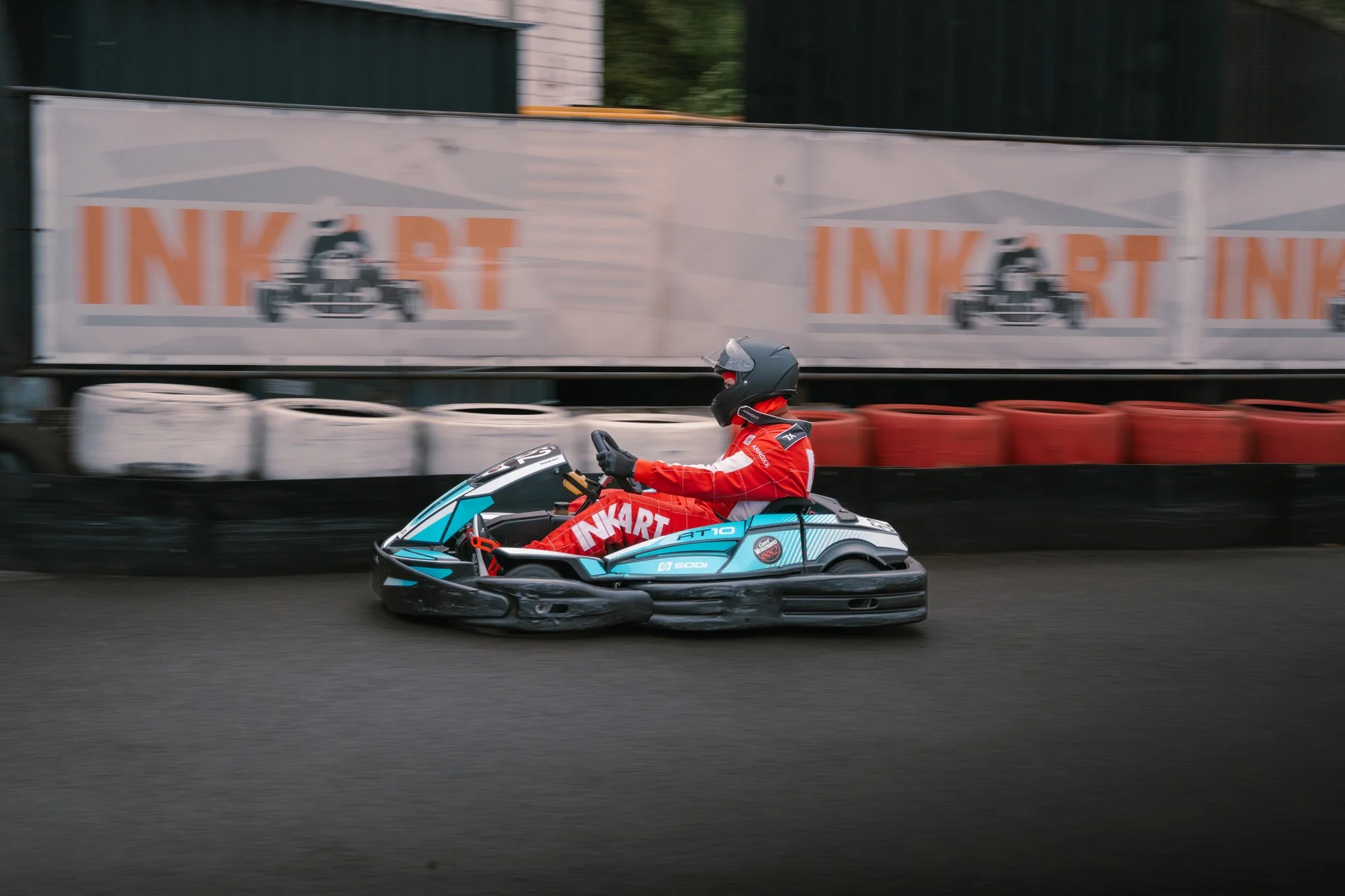 A person in red racing gear and a black helmet driving a go-kart on a race track.