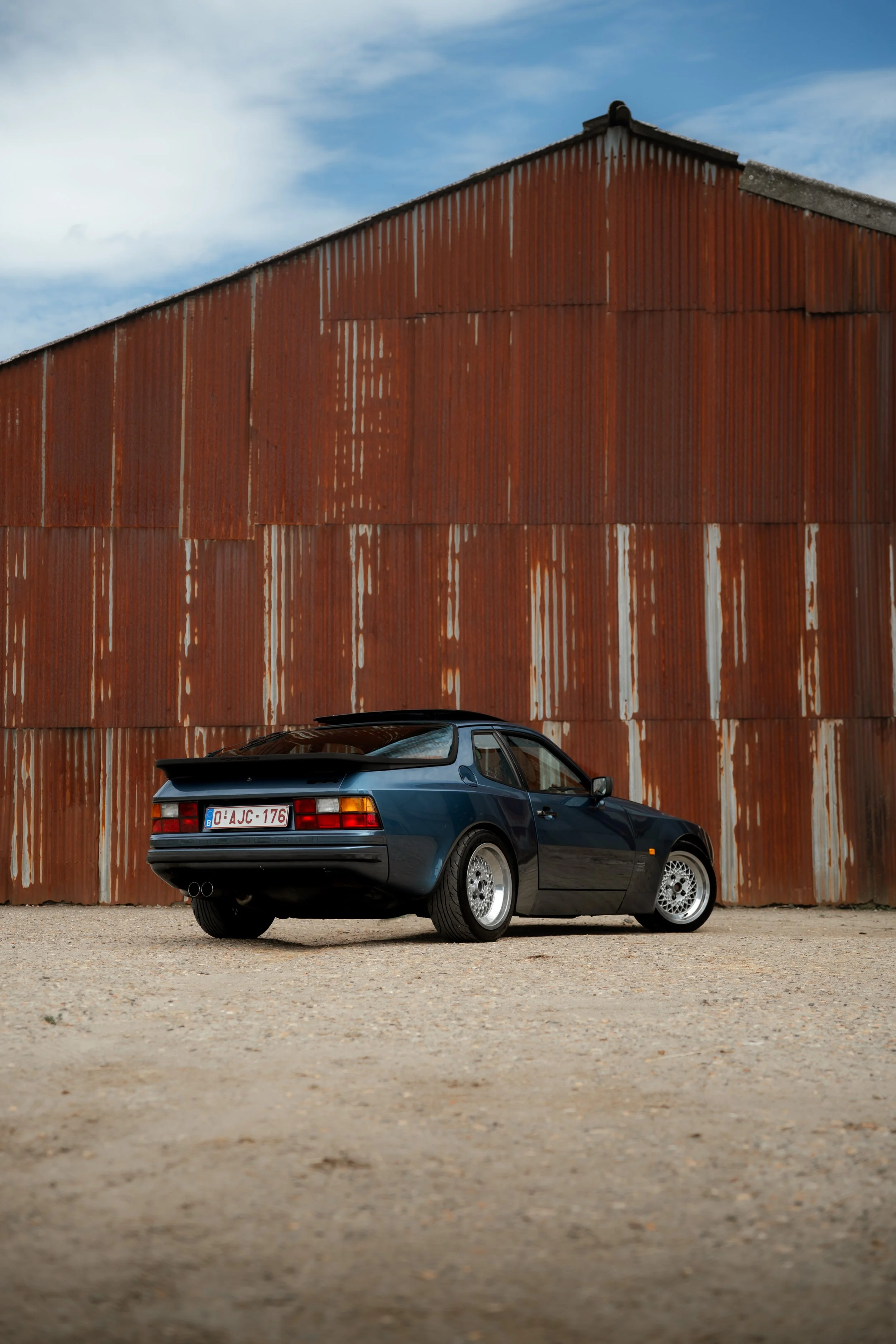 A black sports car parked in front of a large red corrugated metal building under a cloudy sky.