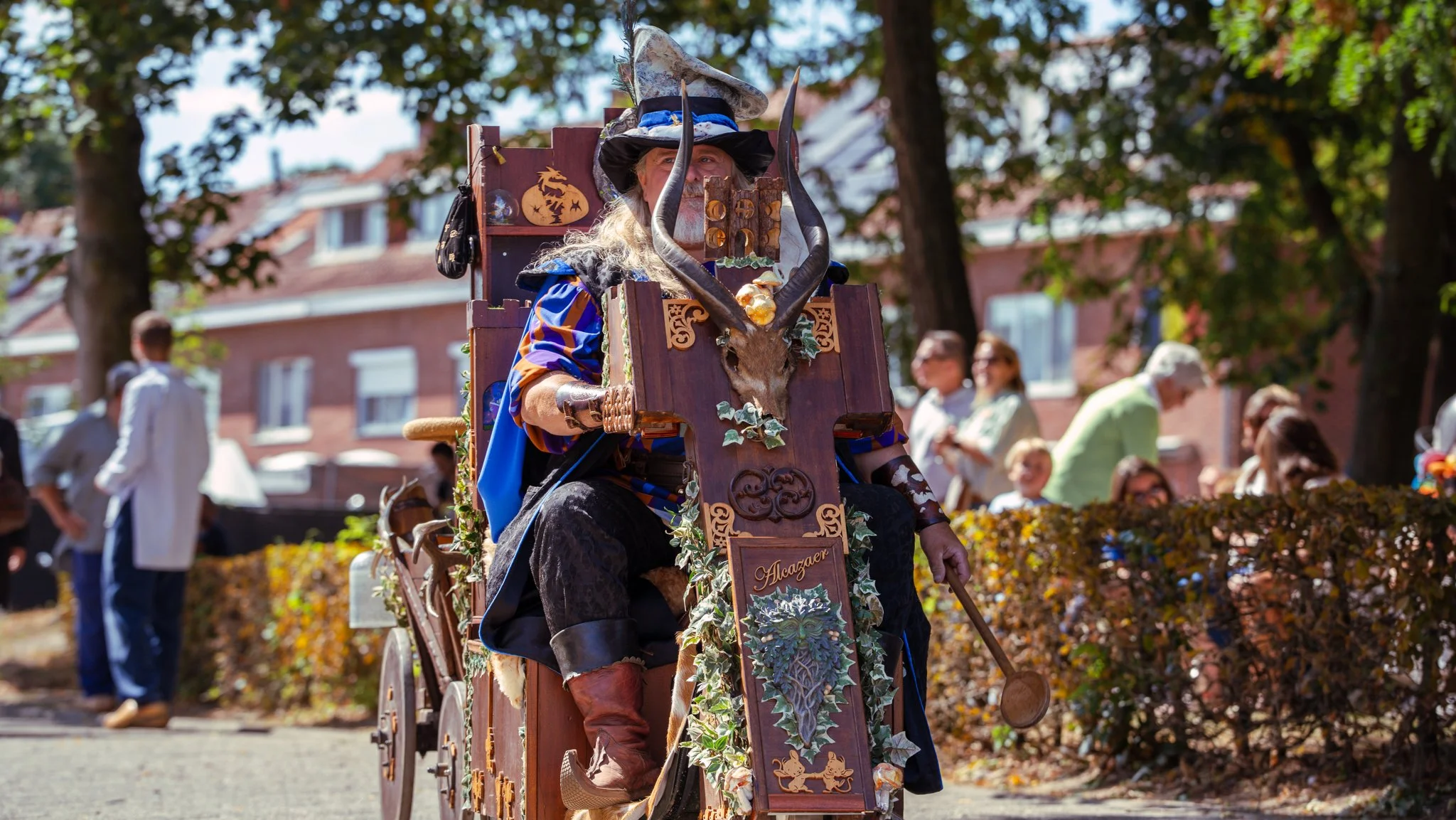 A person in medieval costume riding a decorated wooden cart with dragon and leaf motifs during a festival or parade.