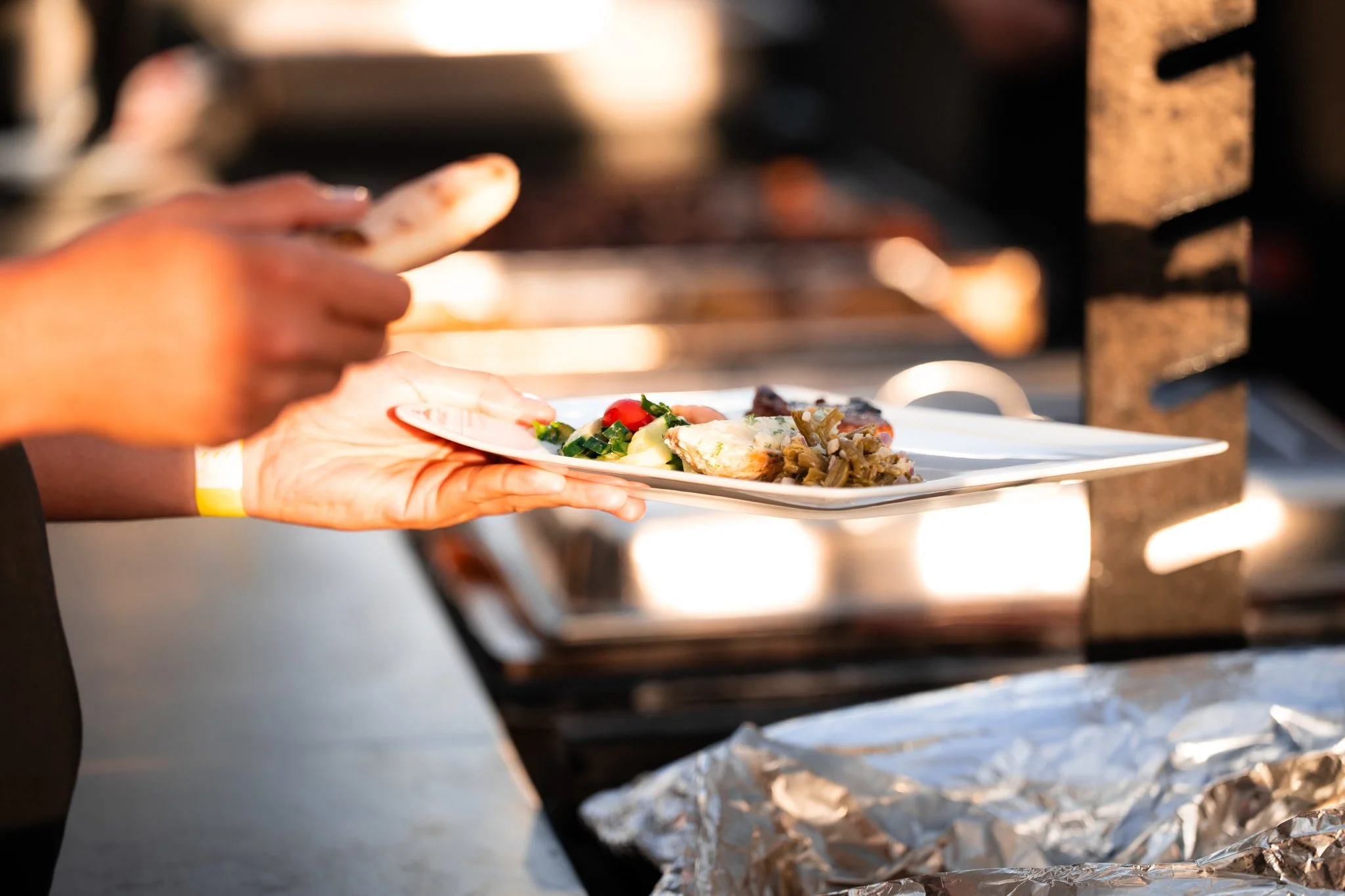 Person serving food onto a white plate at a buffet with a chafing dish in the background