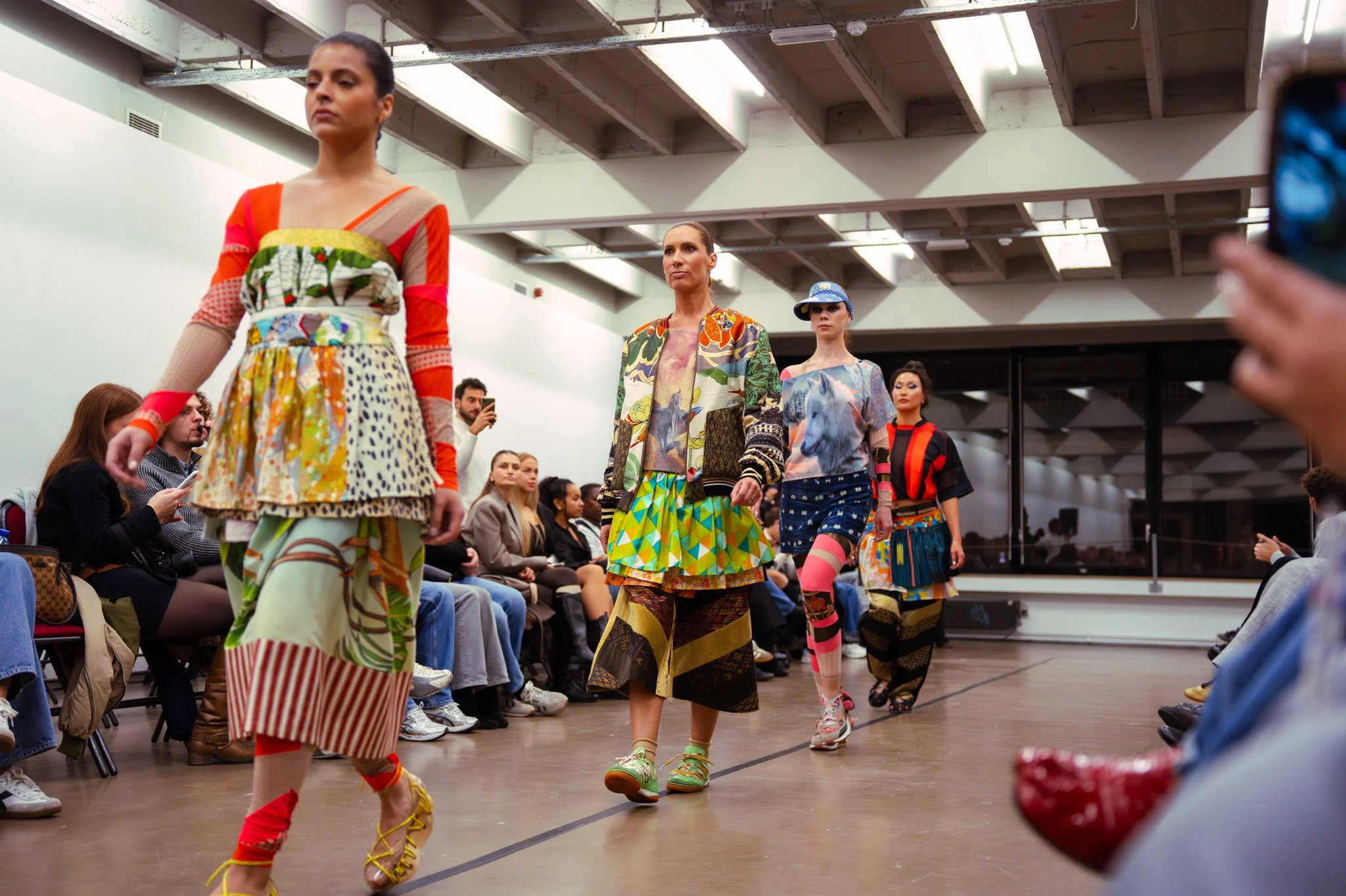 Models walking on the runway during a fashion show, wearing colorful and patterned clothing.