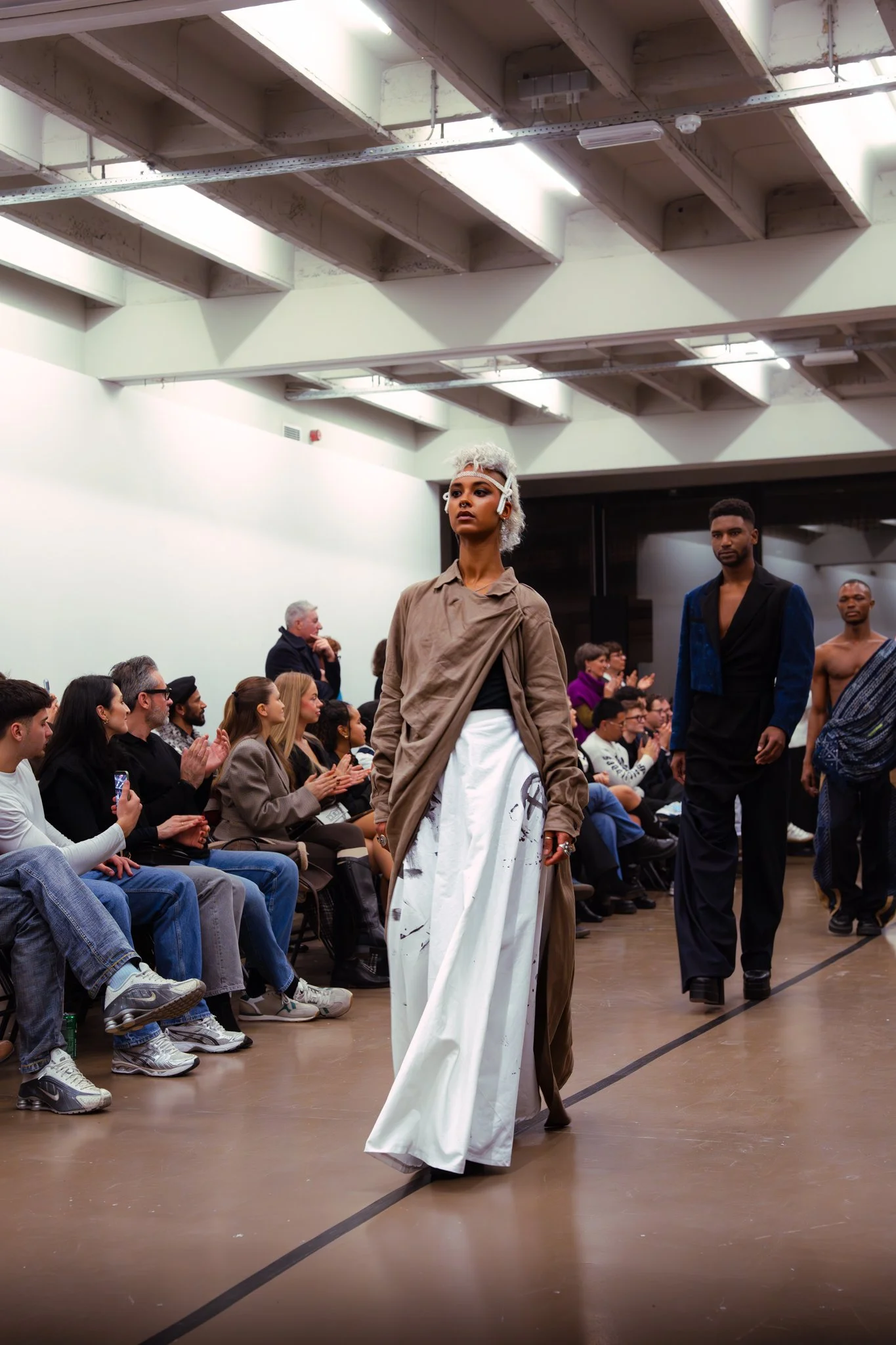 Fashion models walking on runway during a fashion show with seated audience watching.