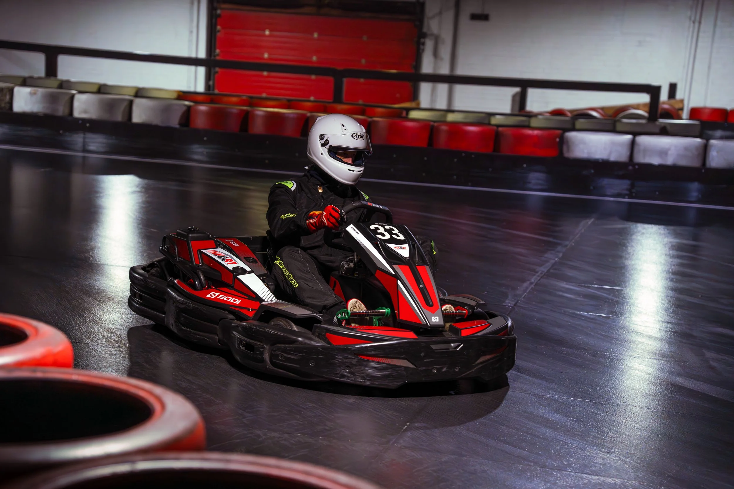 A person wearing a helmet and racing suit driving a red go-kart on an indoor track.