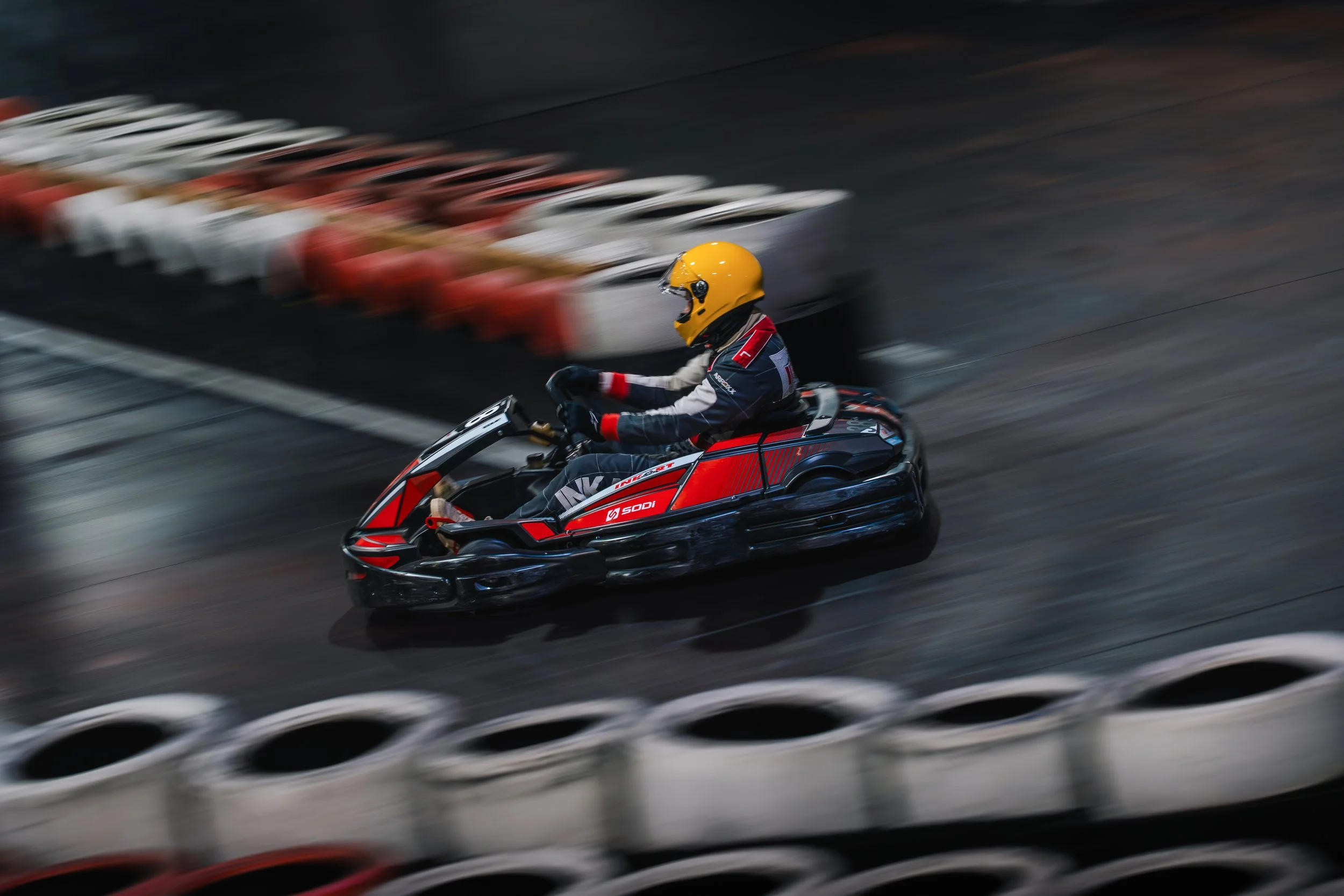 A person in racing gear and yellow helmet riding a red and black snowmobile on a dark, motion-blurred track.
