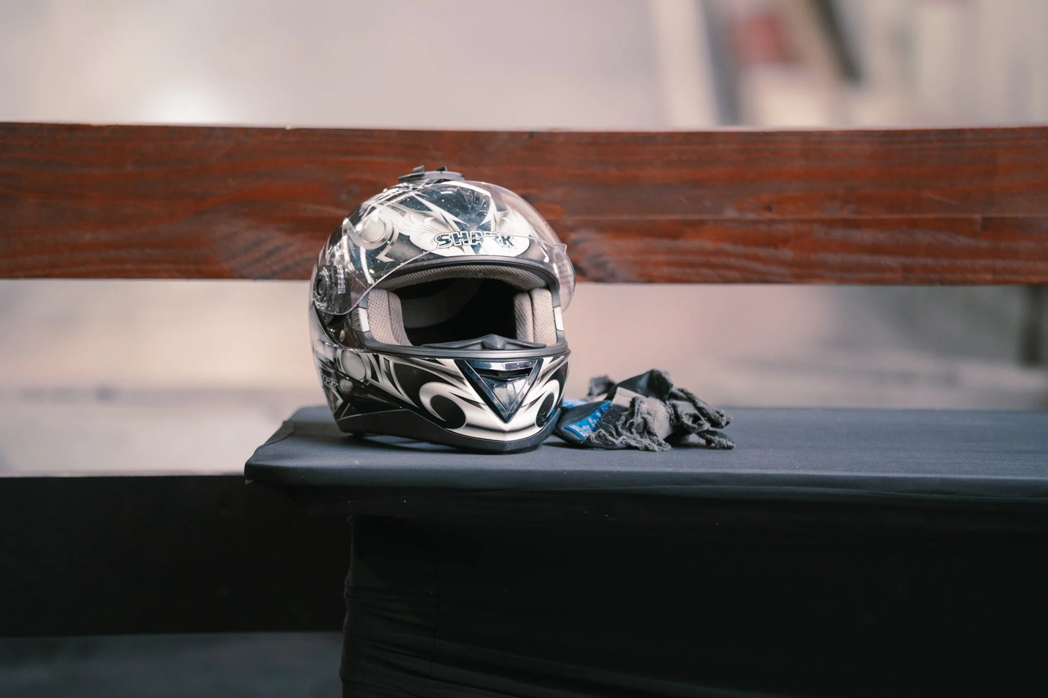 Motorcycle helmet and gloves on a black padded surface with a wooden backrest behind.