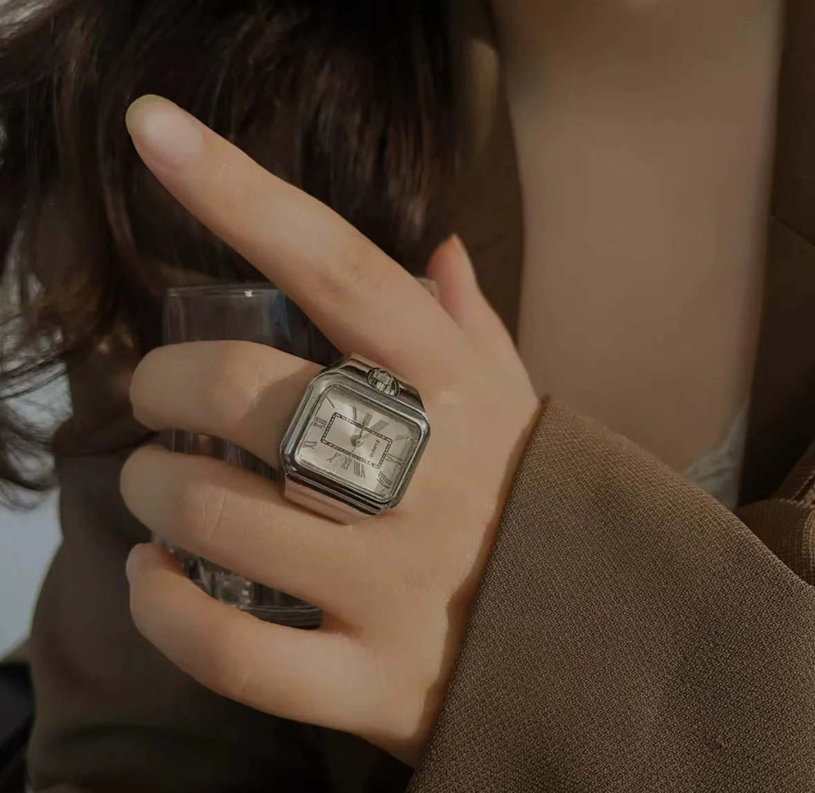 Person holding a glass of beverage and wearing a large silver watch with Roman numerals.
