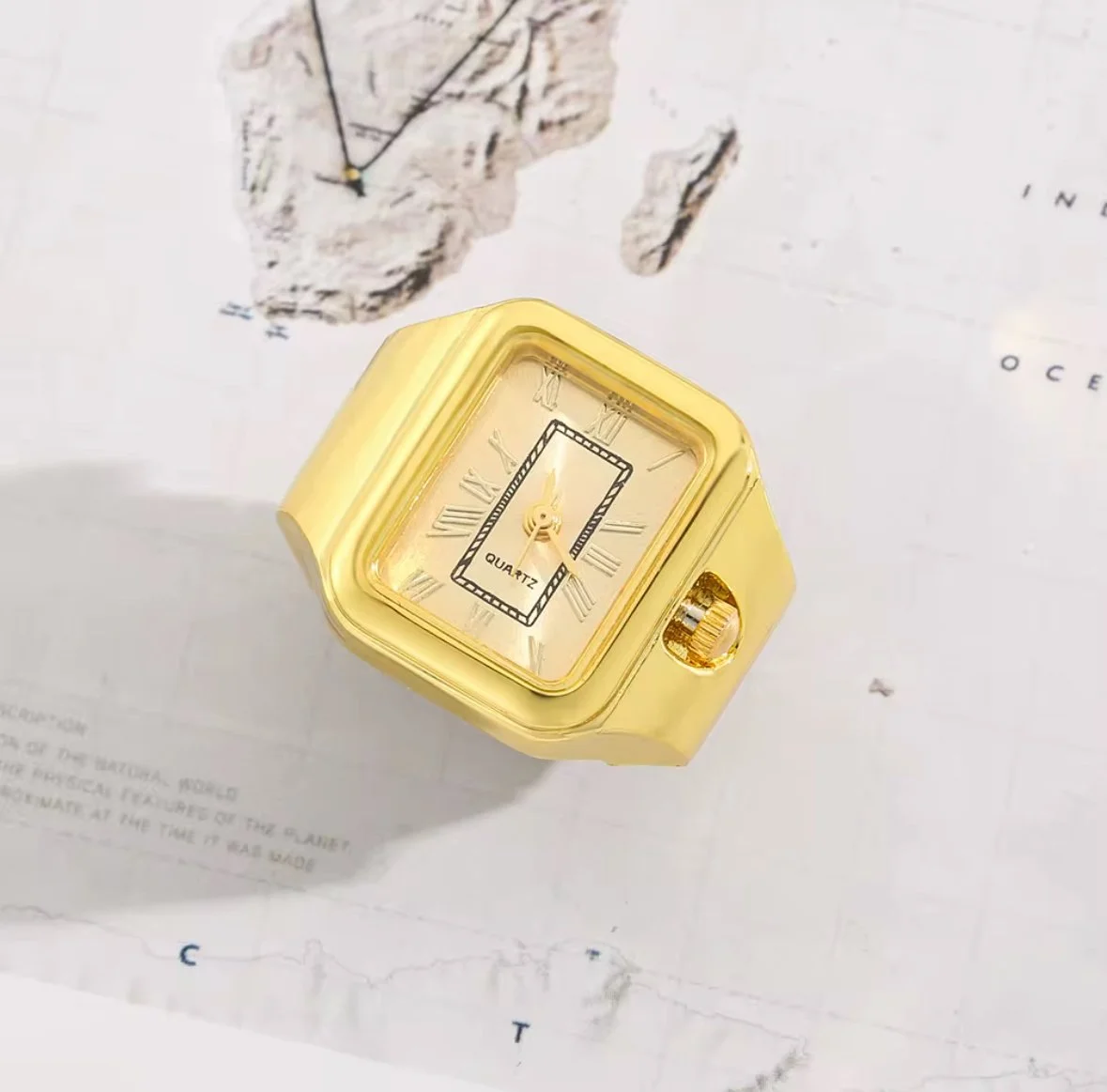 Gold-colored quartz finger watch with Roman numerals, placed on a sheet of paper.