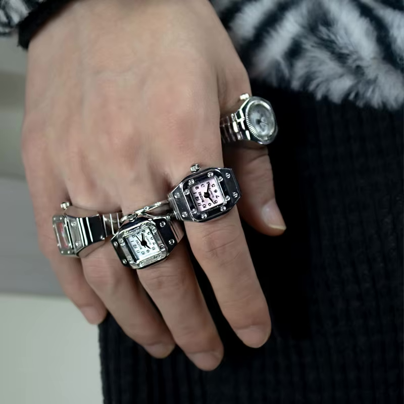 Close-up of a man’s hand wearing stacked TinyTime ring watches in Pixie and Tinker styles. Featuring black, silver, and pink square dials with riveted bezels. Perfect for Y2K, unisex fashion lovers, and modern jewelry collectors.