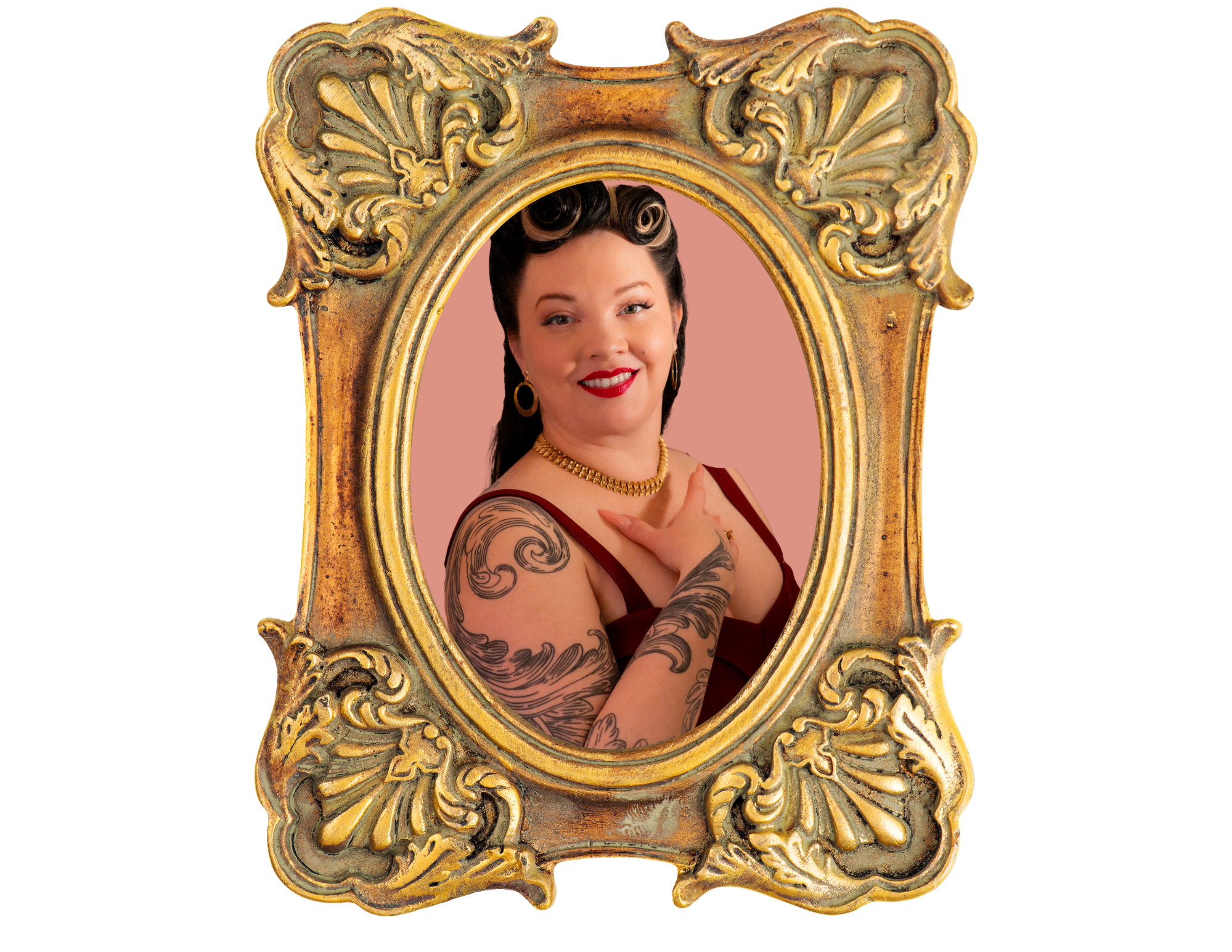 A woman with tattoos on her arms, smiling, wearing a red dress and gold jewelry, looking at herself in an ornate gold mirror.