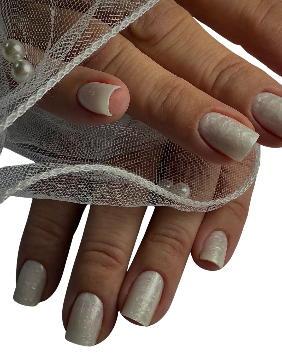 Close-up of a person's hand with white gel polish manicure and Russian manicure, decorated with a sheer fabric adorned with pearls.