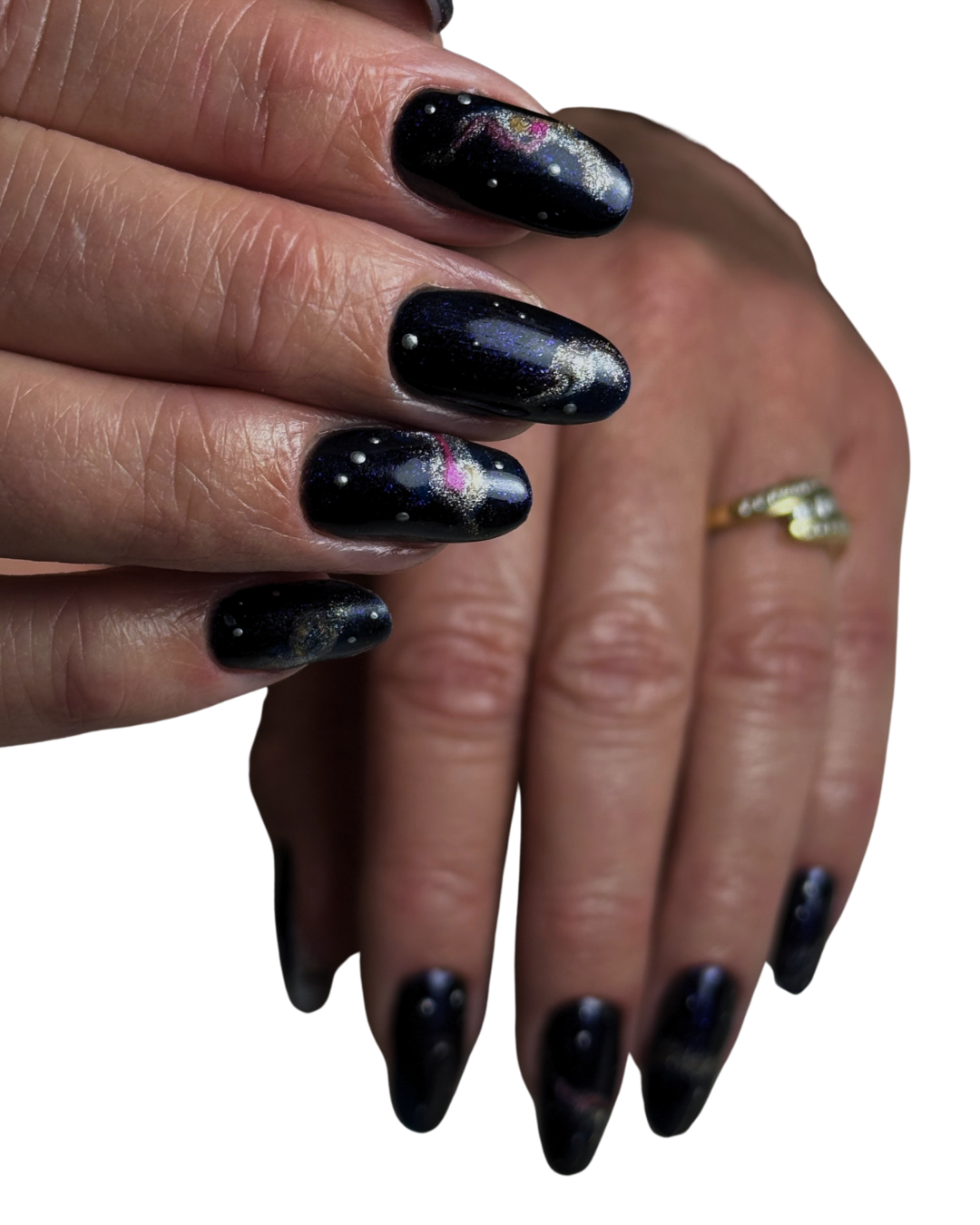 Close-up of a person's hand with galaxy-themed black nail polish featuring white dots and pink, blue, and gold accents, and a gold ring on the ring finger.