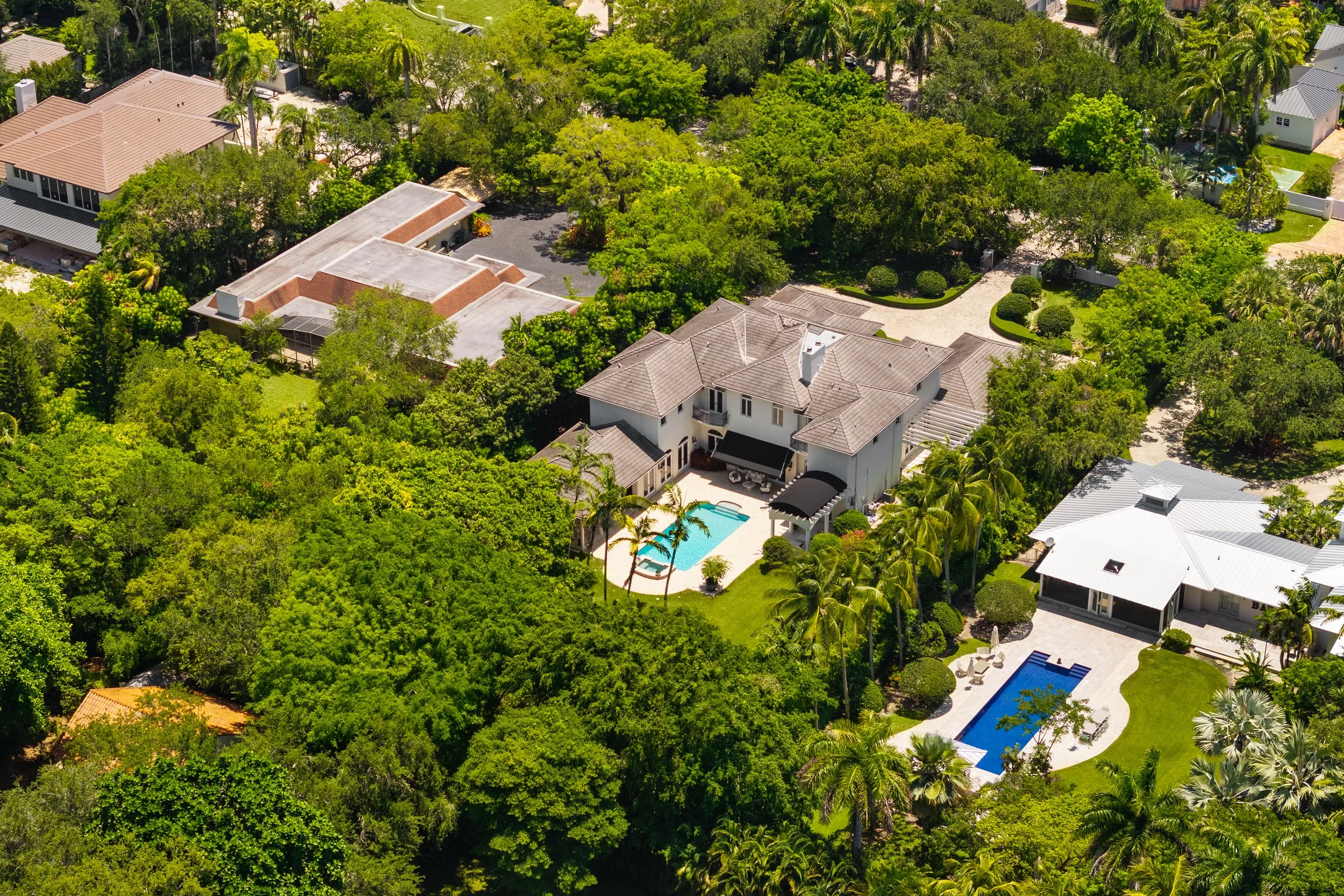 Aerial view of a large residential property with multiple swimming pools, surrounded by lush green trees and landscaping.