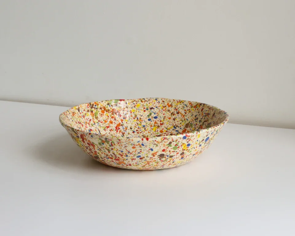 Colorful speckled ceramic bowl placed on a plain white surface against a light background.