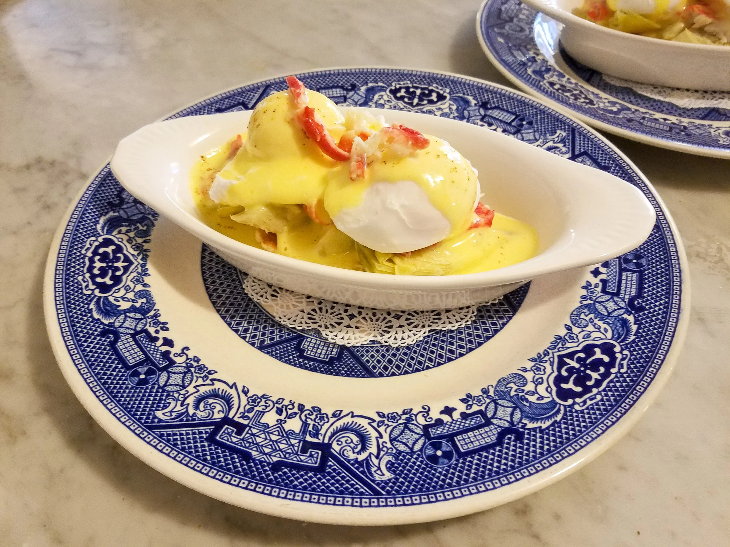 Poached eggs topped with hollandaise sauce, served on a white dish with a blue patterned border.