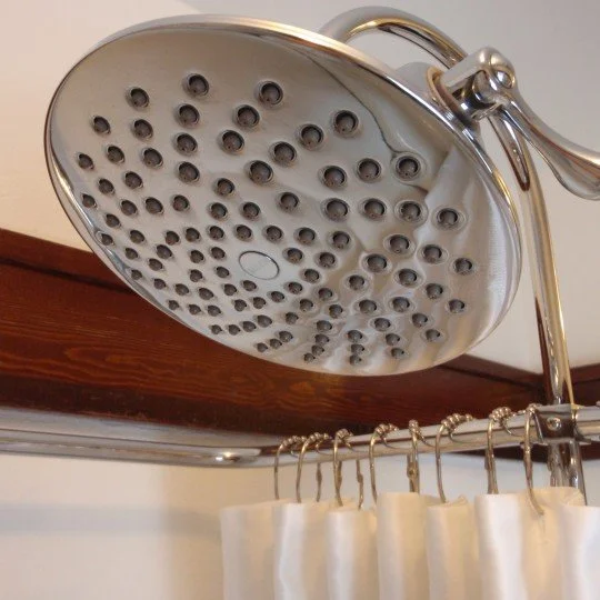 Close-up of a showerhead attached to a metal pipe, with a curtain rod and beige shower curtain below.