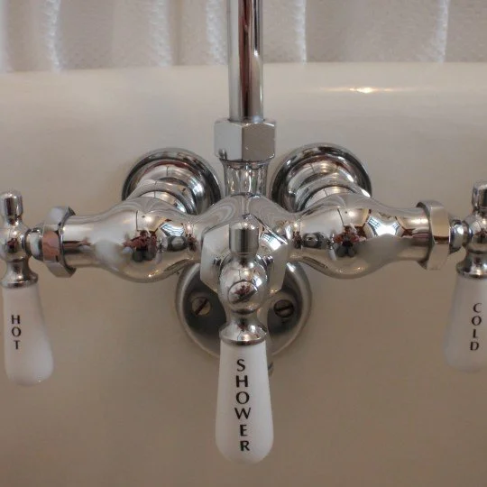 Close-up of a vintage-style bathroom faucet with three handles labeled HOT, SHOWE, and COLD, mounted above a white bathtub.