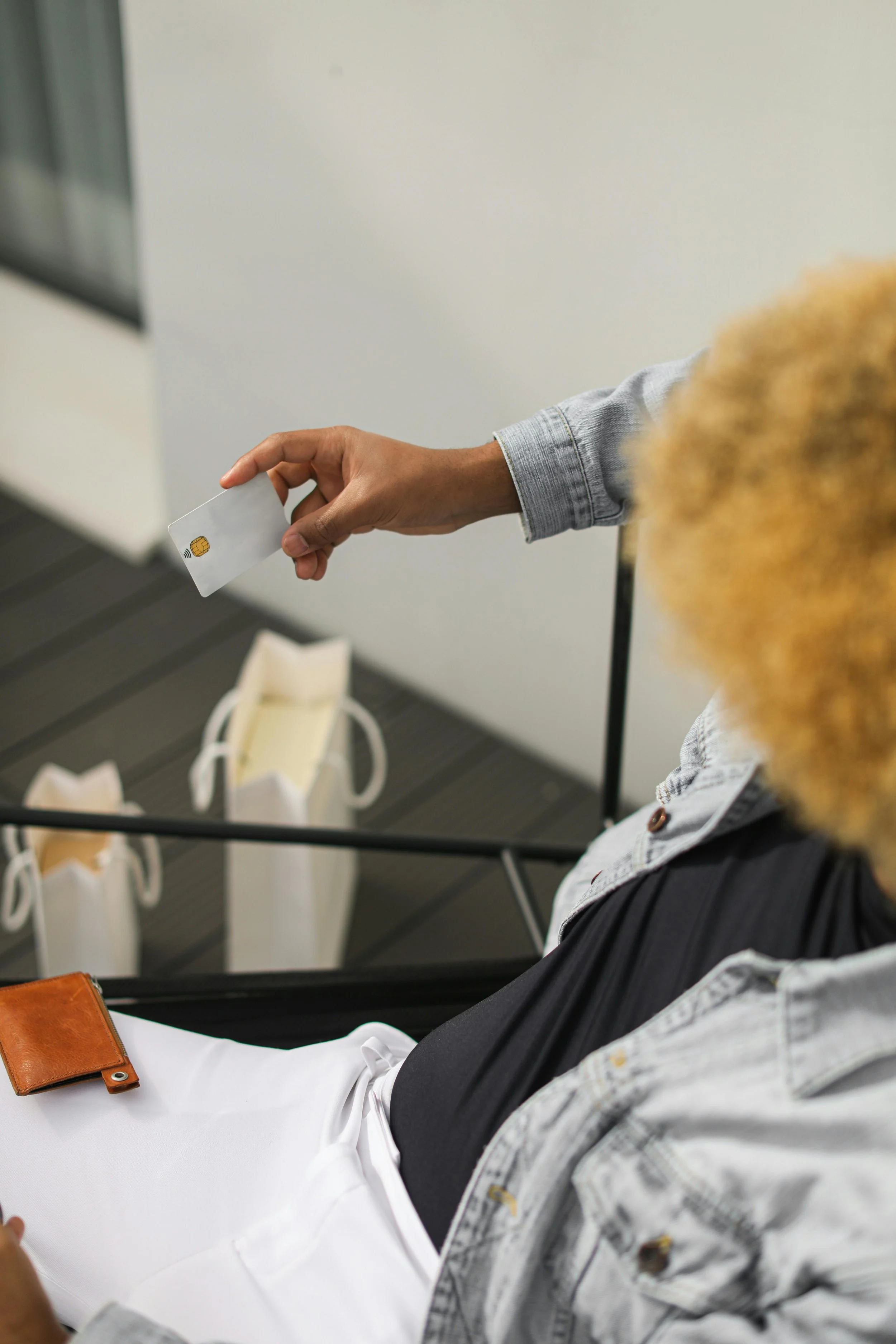 Une personne tenant une carte de crédit à proximité d'une autre personne assise, avec plusieurs sacs blancs en arrière-plan.