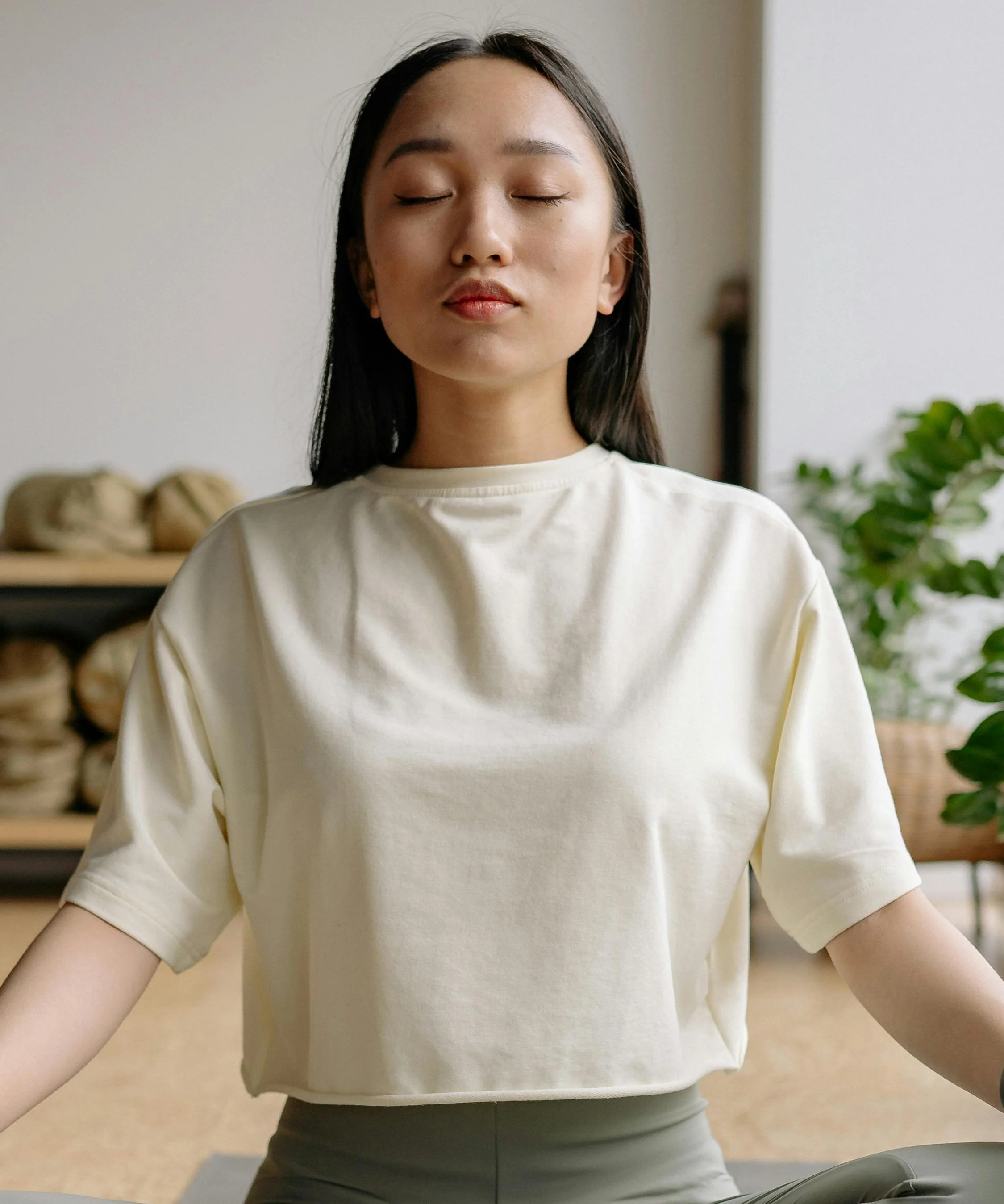 A woman practicing breathing with eyes closed in a bright indoor space.