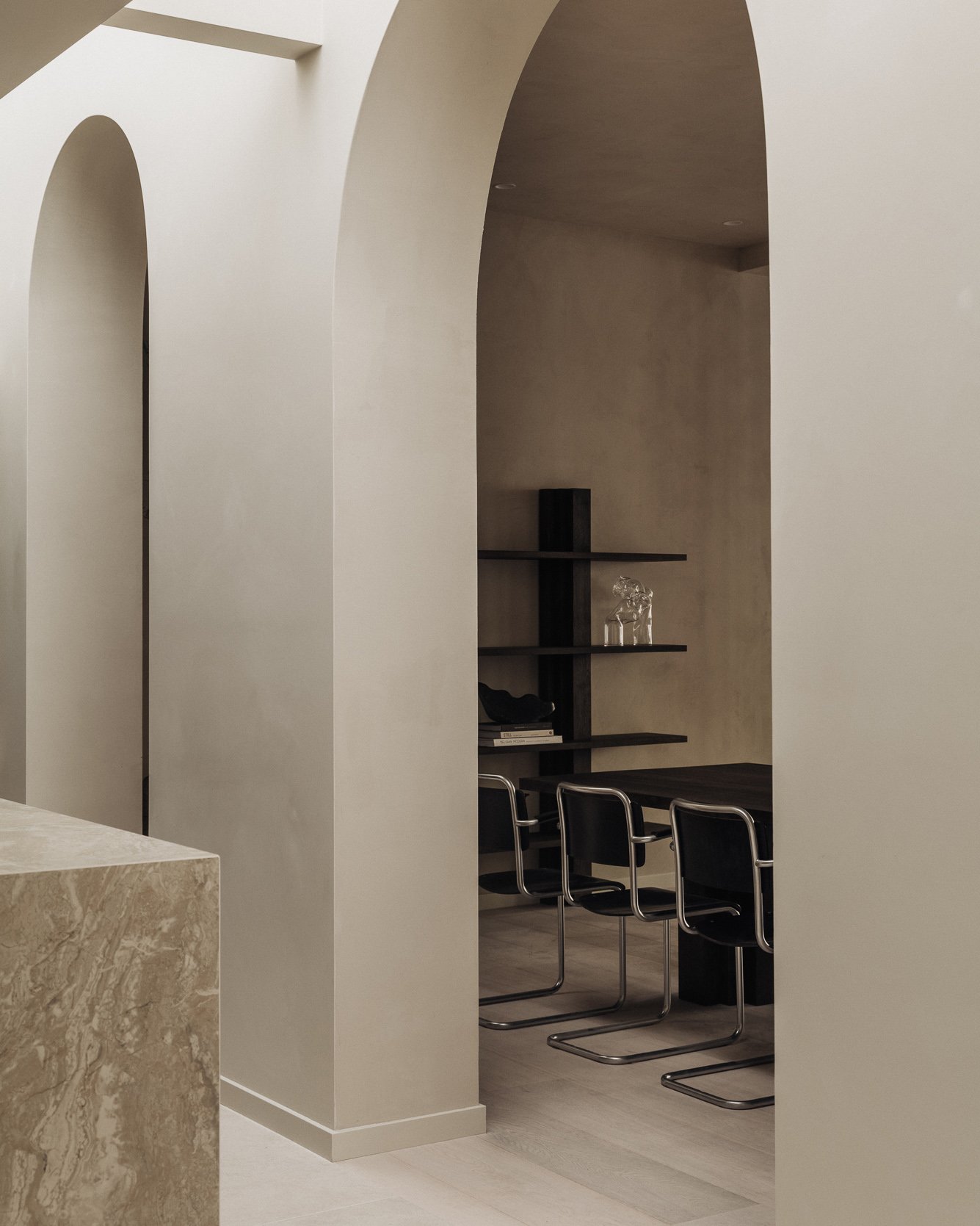 Interior space with archways, a desk, and black chairs with metal frames, minimalist design.