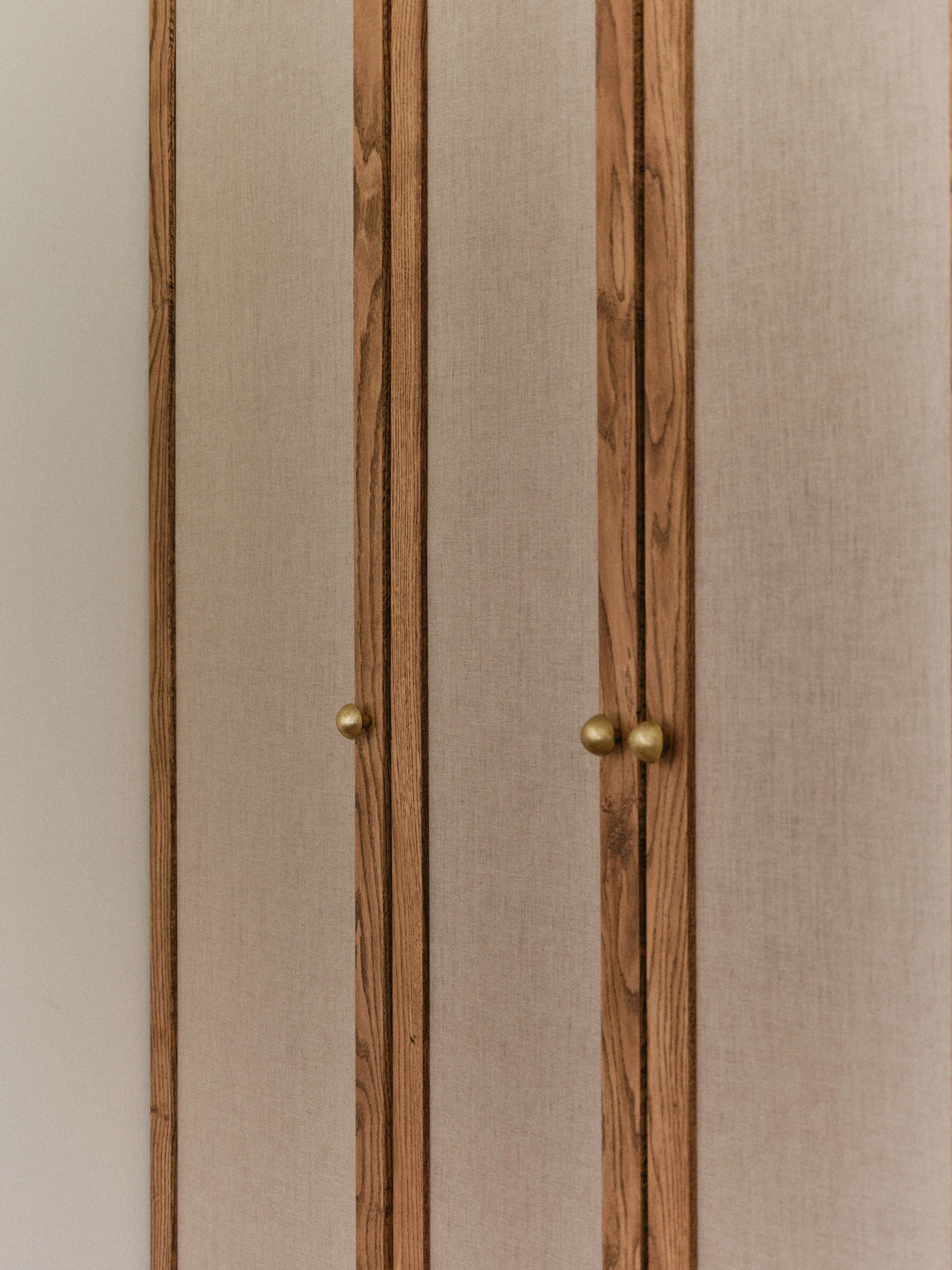 A wooden closet with beige fabric panels and round gold handles.