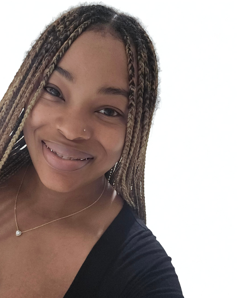 Close-up selfie of a young woman with braided hair, smiling, wearing a black top, a nose piercing, and a delicate necklace, against a plain white background.