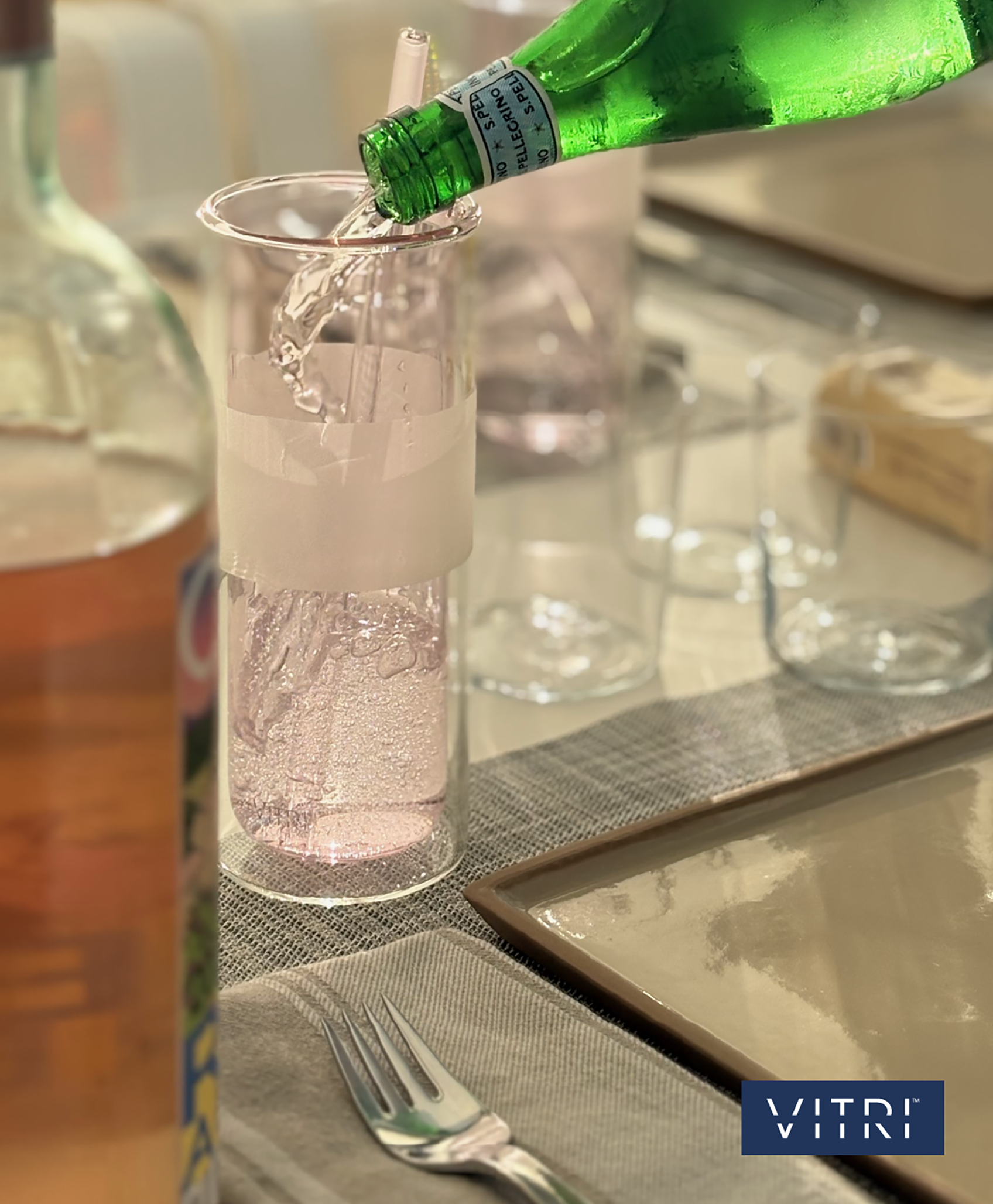 Sparkling water being poured into a tall light‑pink glass at a casual dinner table setting
