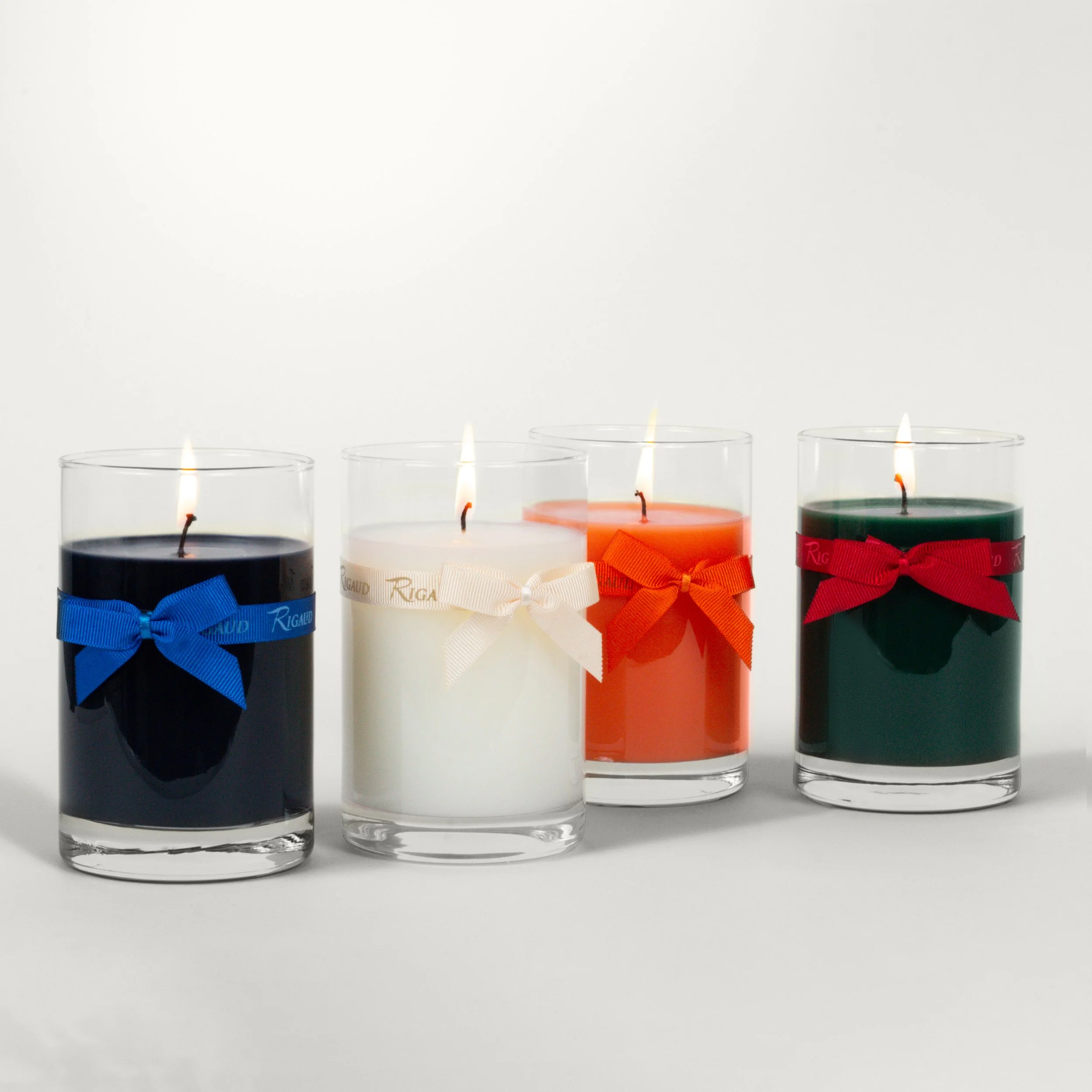 Four glass candle votives arranged in a staggered row, each wrapped with bright, colorful bows.